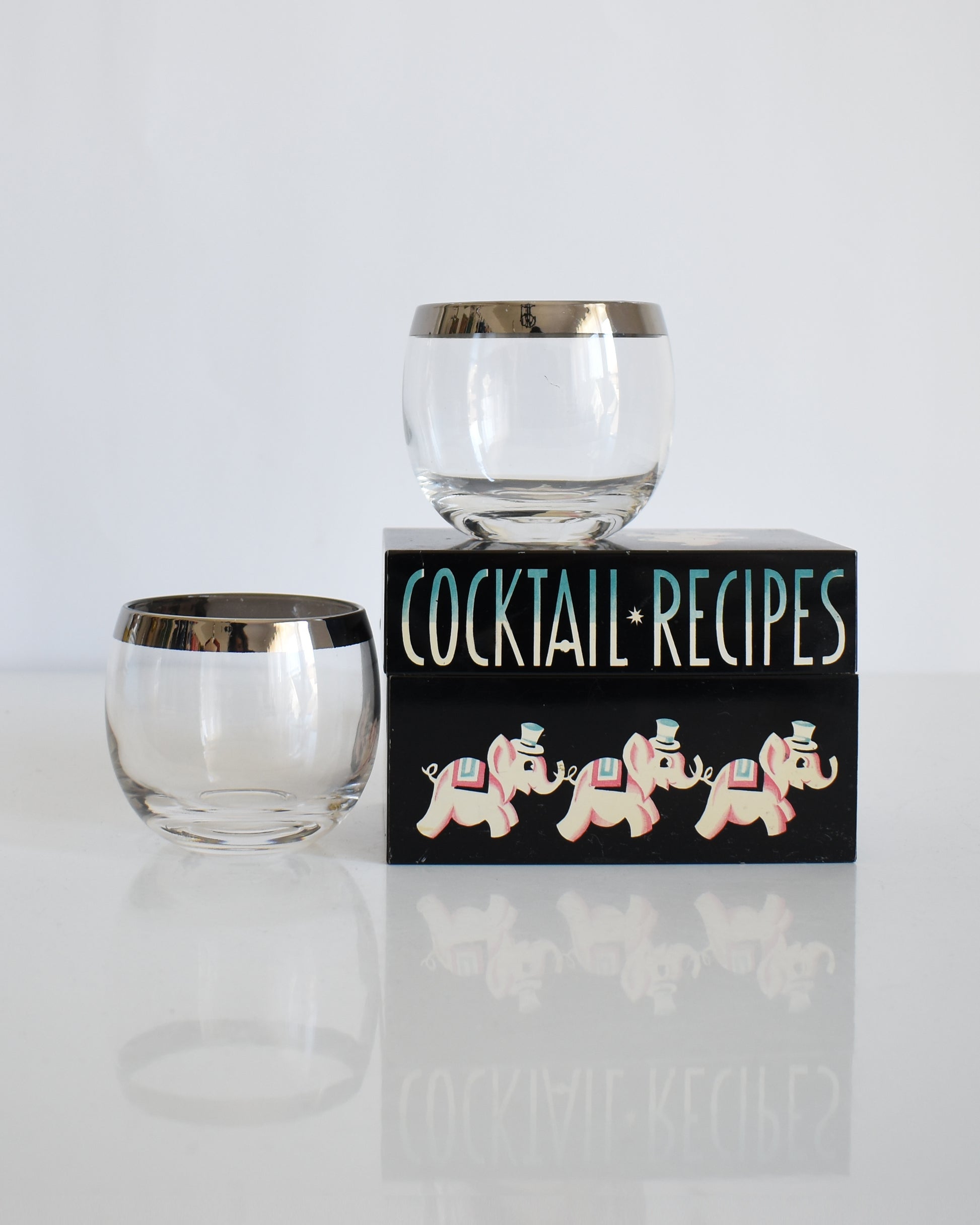 A pair of 1960's vintage Dorothy Thorpe inspired style roly poly glasses. One of the glasses is on a cocktail box