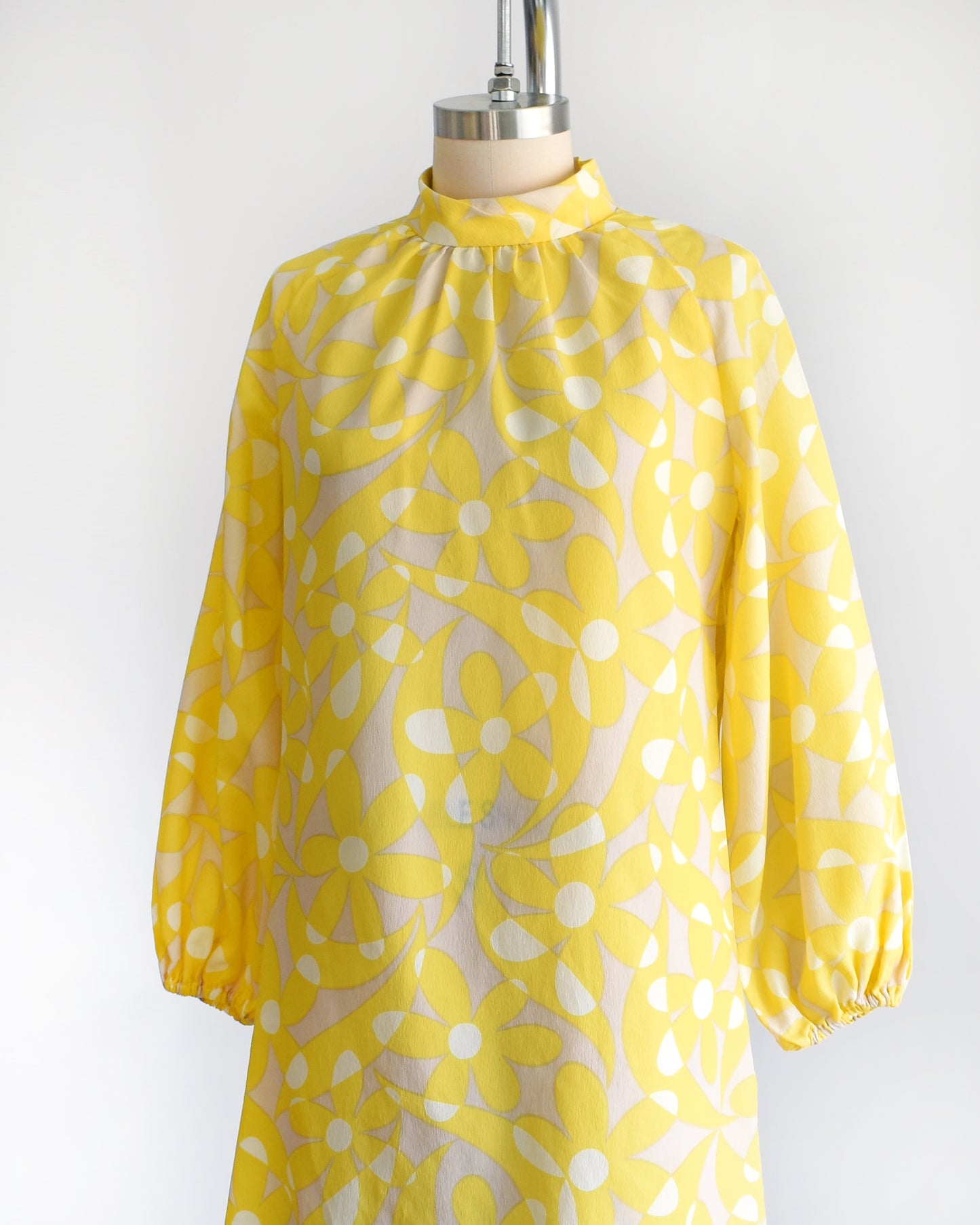 Side front view of a vintage 1960s mod mini dress features a bright yellow and white floral pattern with swirls, set on a pale beige background. 