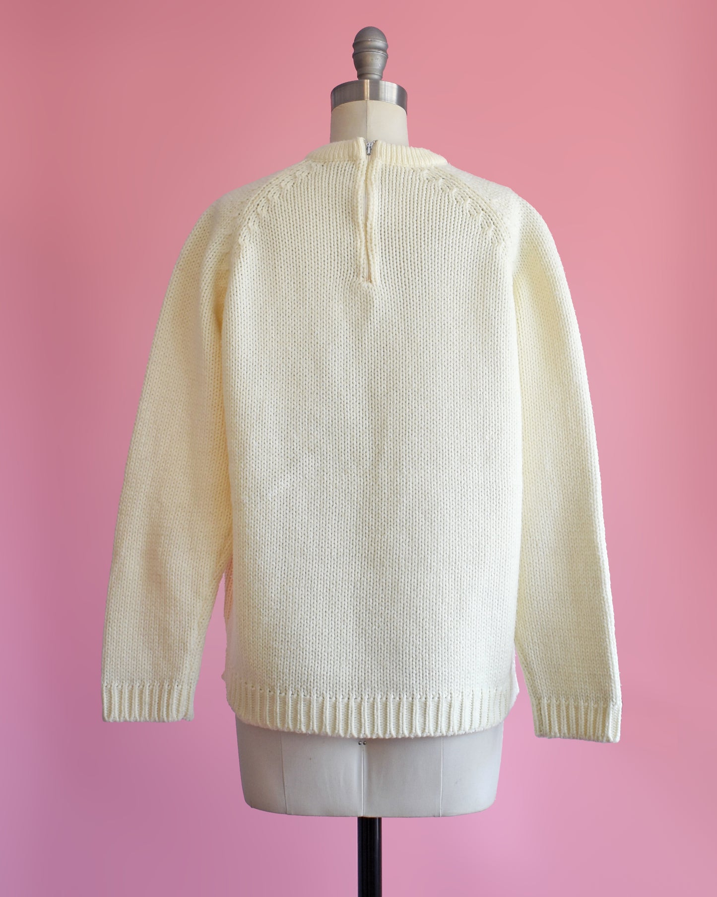 back view of  a vintage 1970s white sweater with red and blue floral pattern on a mannequin against a pink background