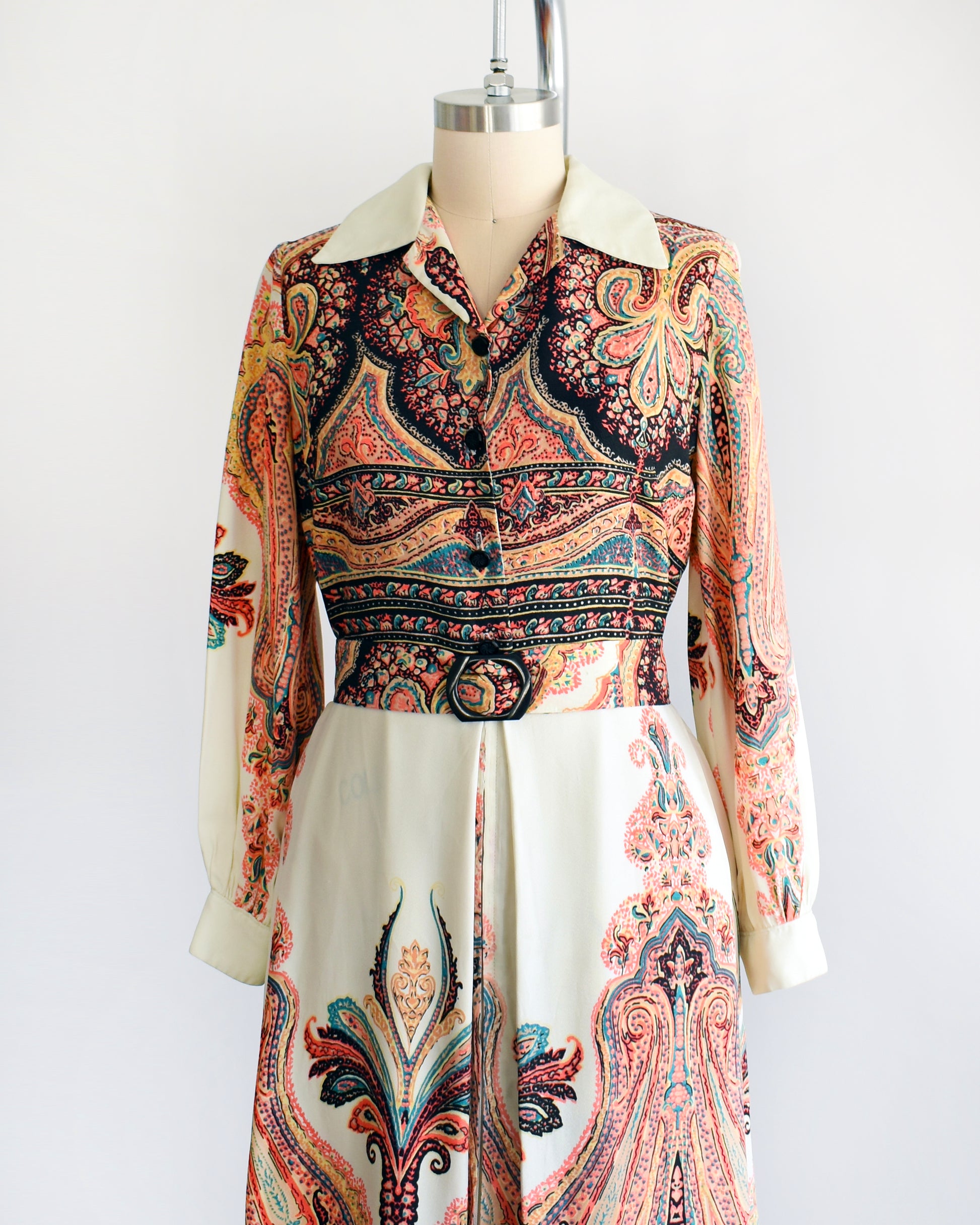 Side front view of a vintage 1970s psychedelic paisley maxi dress with button front and matching belt that has a black buckle.