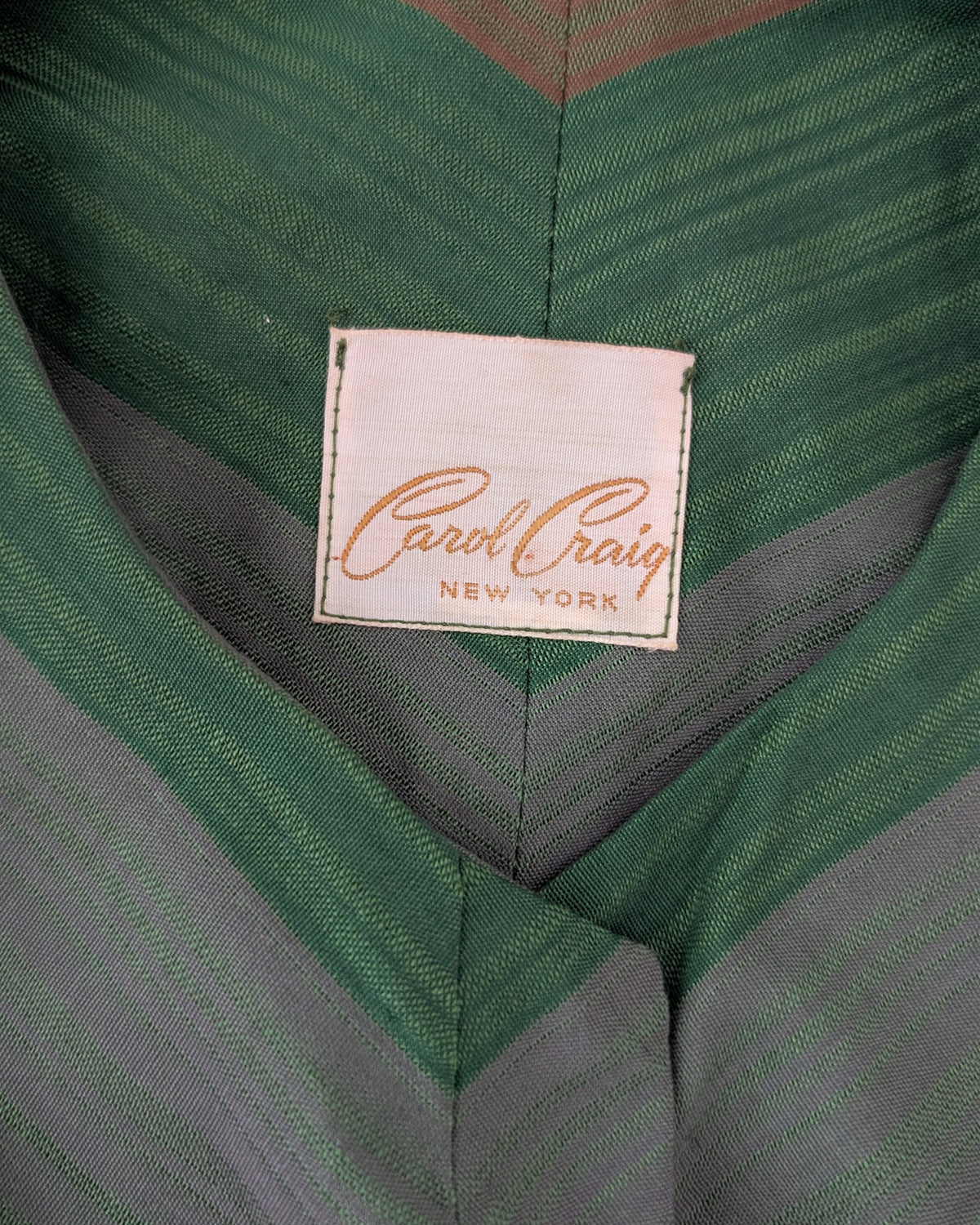 Close-up of a green and gray striped garment with a visible sewn-in label reading Carol Craig New York.