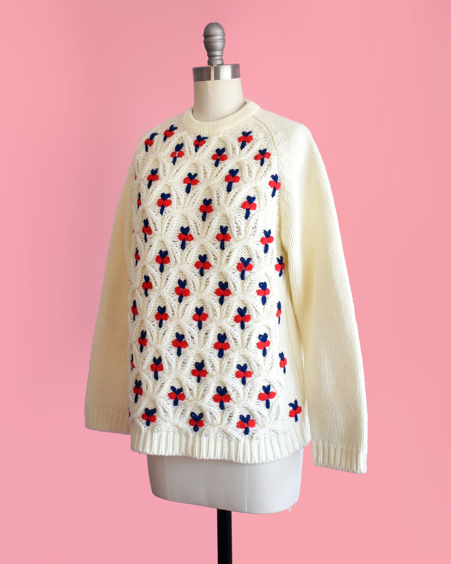 side front view of  a vintage 1970s white sweater with red and blue floral pattern on a mannequin against a pink background