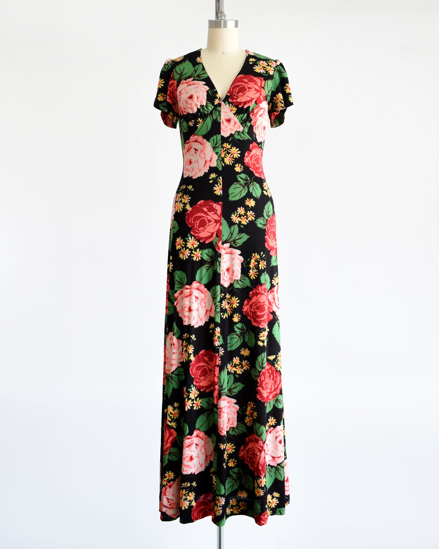 A vintage 1970s black floral maxi dress features a vibrant floral pattern of red and pink roses, green leaves, and yellow and orange daisies. 
