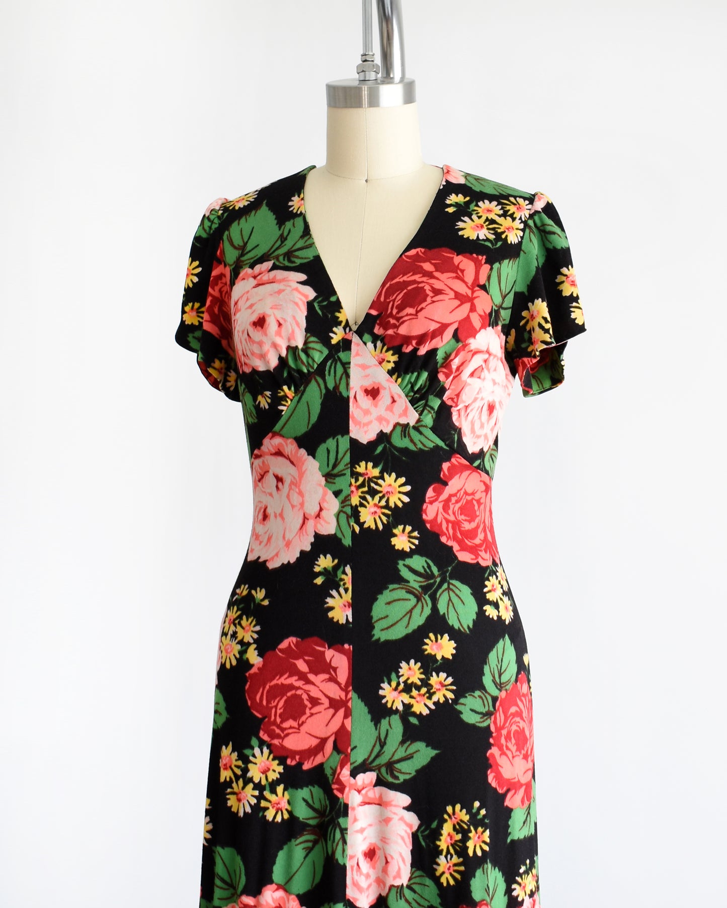 Side front view of a vintage 1970s black floral maxi dress features a vibrant floral pattern of red and pink roses, green leaves, and yellow and orange daisies. 