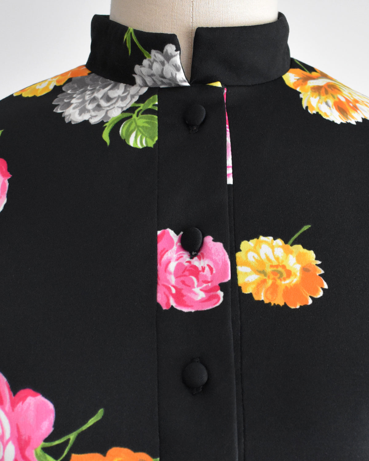 close up of the bodice of a vintage 1970s black two-piece suit set with a colorful floral print, displayed on a mannequin against a plain white background. 