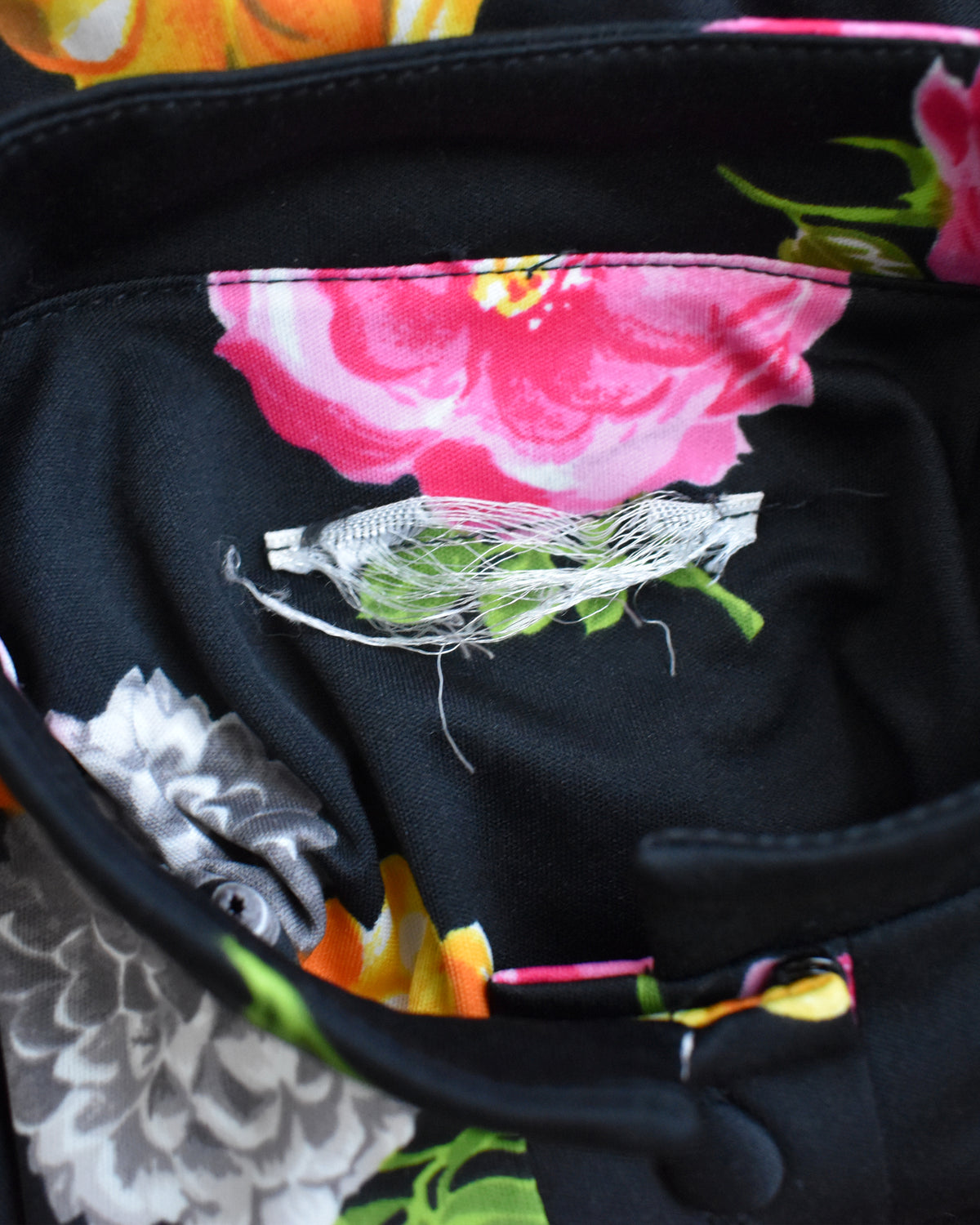 close up of the frayed tag on a vintage 1970s black two-piece suit set with a colorful floral print, displayed on a mannequin against a plain white background.
