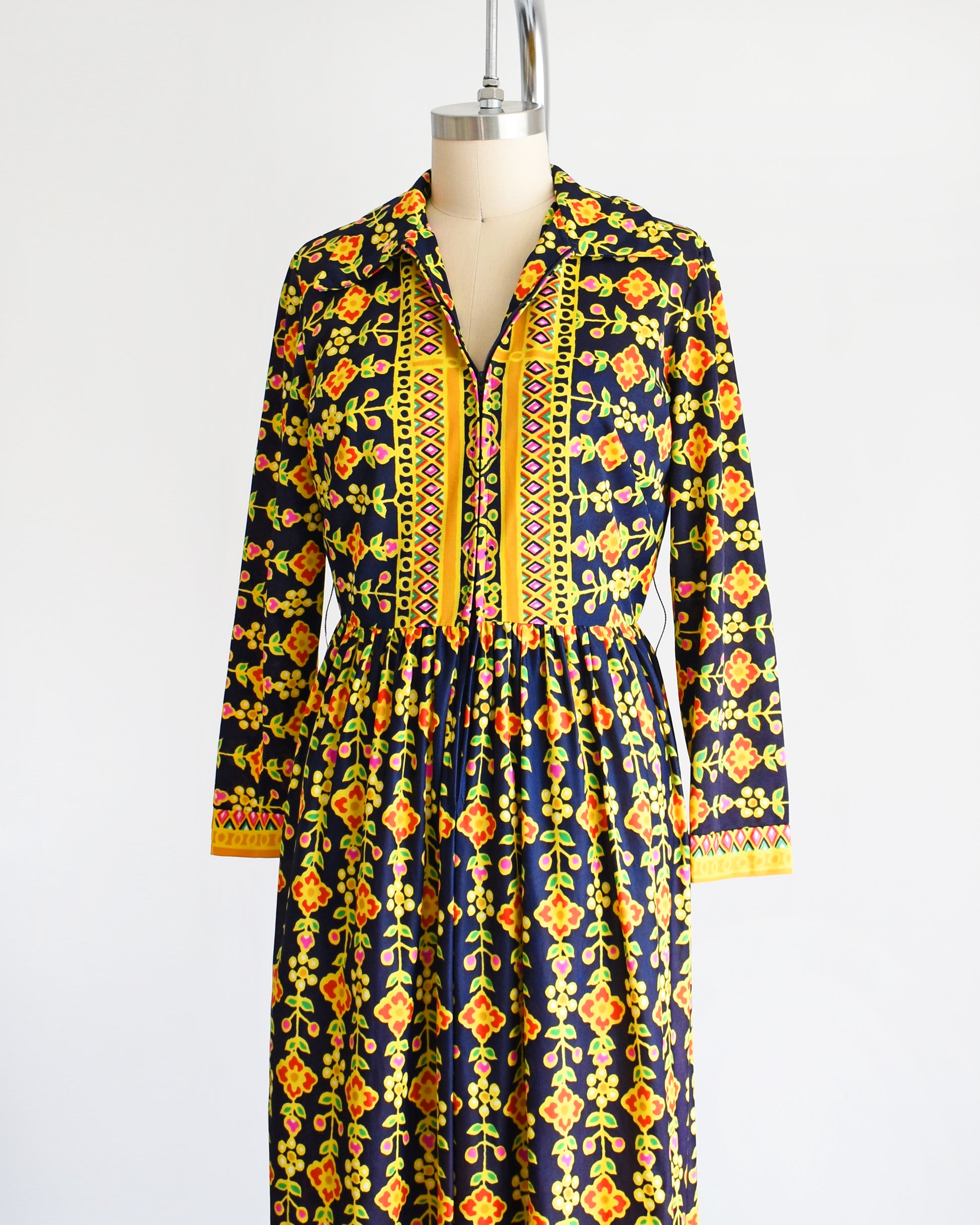 Side front view of a vintage 1970s navy blue maxi dress with a colorful striped floral print. The front zipper is partially unzipped.