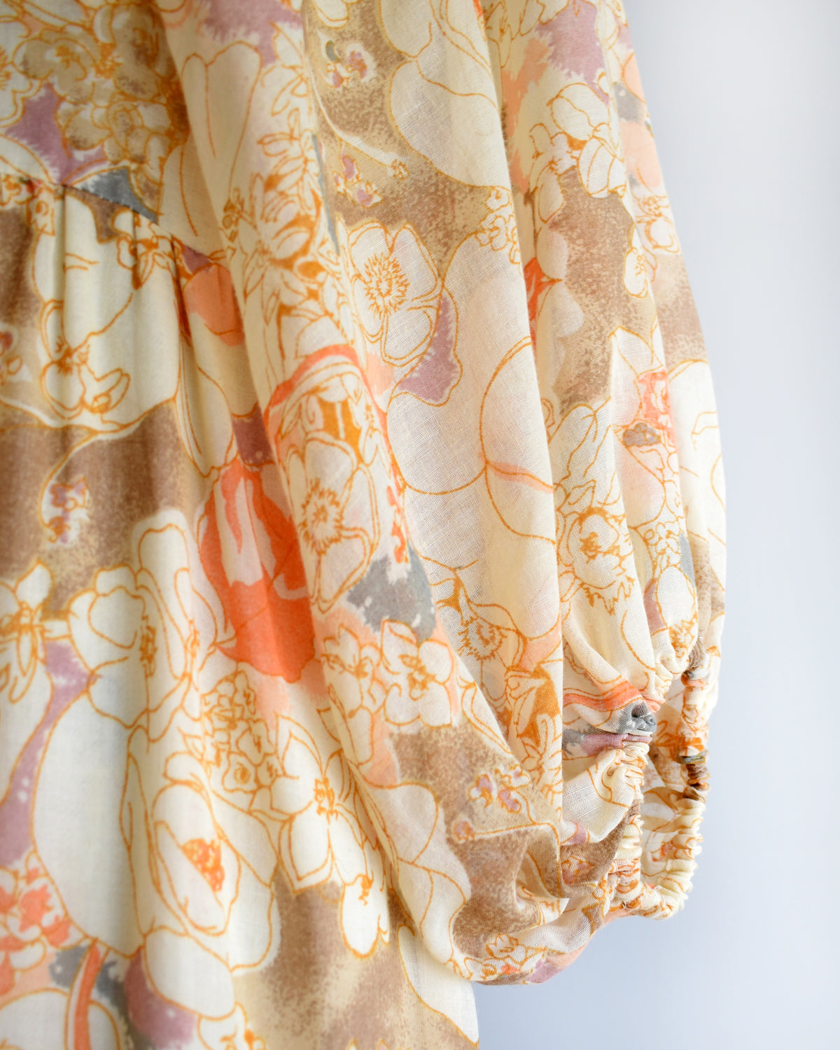 close up of the balloon sleeves on a vintage 1970s orange floral lace maxi dress on a dress form against a white background