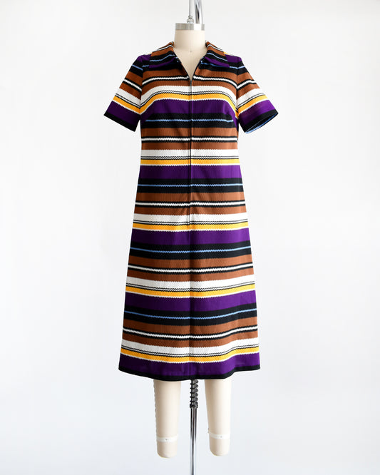 Front view of a vintage 1970s striped mod dress that has black, brown, white, blue, yellow, and purple horizontal stripes with zigzag edges. The dress features a zipper down the front which is unzipped a little bit in this photo.
