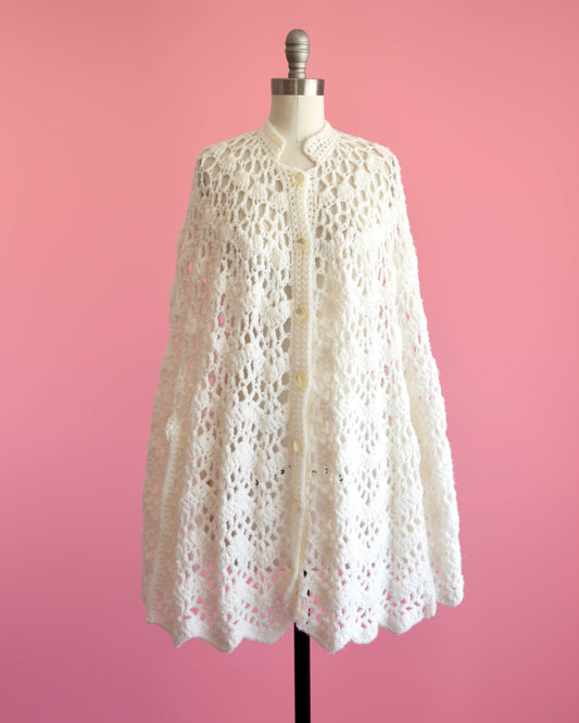 A vintage 1970s white crochet poncho that has a small collar, button down front and arm slits on each side of the poncho.
