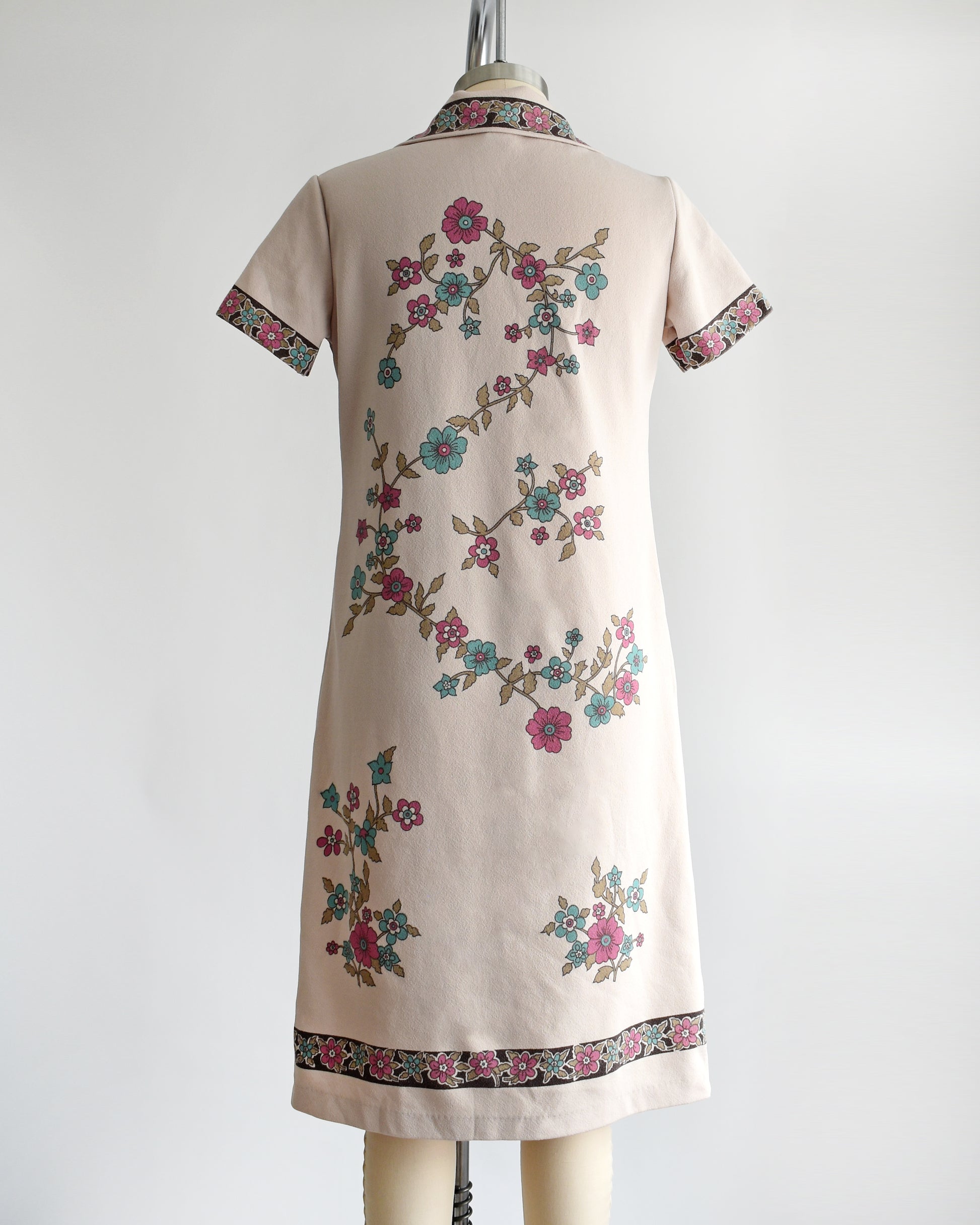 Back view of a vintage 1970s light brown mod dress with button front that features a blue and pink floral print 