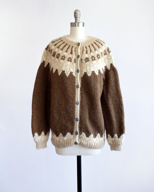 A vintage 1970s brown cardigan that has a dark and light brown and white Fair Isle pattern around the collar, cuffs, and hem, along with silver buttons up the front.