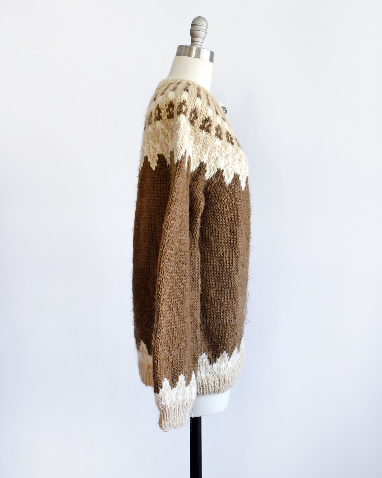 Side view of a vintage 1970s brown cardigan that has a dark and light brown and white Fair Isle pattern around the collar, cuffs, and hem, along with silver buttons up the front.