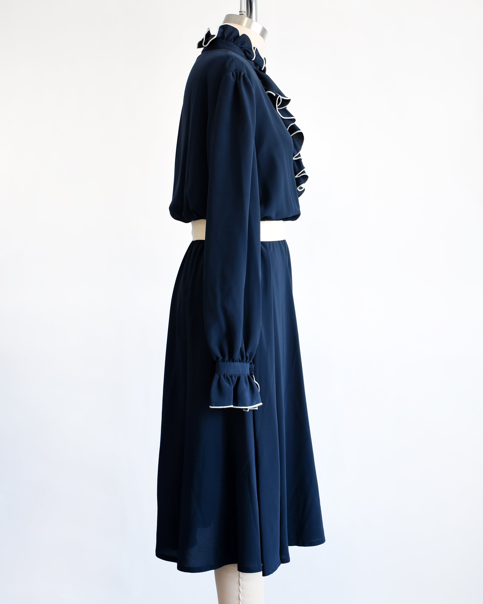 side view of a vintage late 1970s early 1980s navy ruffled dress with cream colored tie belt