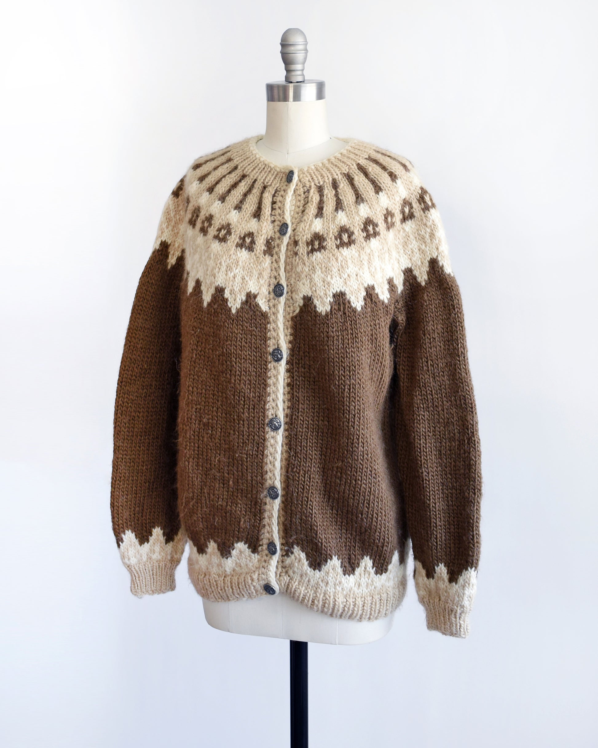 Side front view of a vintage 1970s brown cardigan that has a dark and light brown and white Fair Isle pattern around the collar, cuffs, and hem, along with silver buttons up the front.