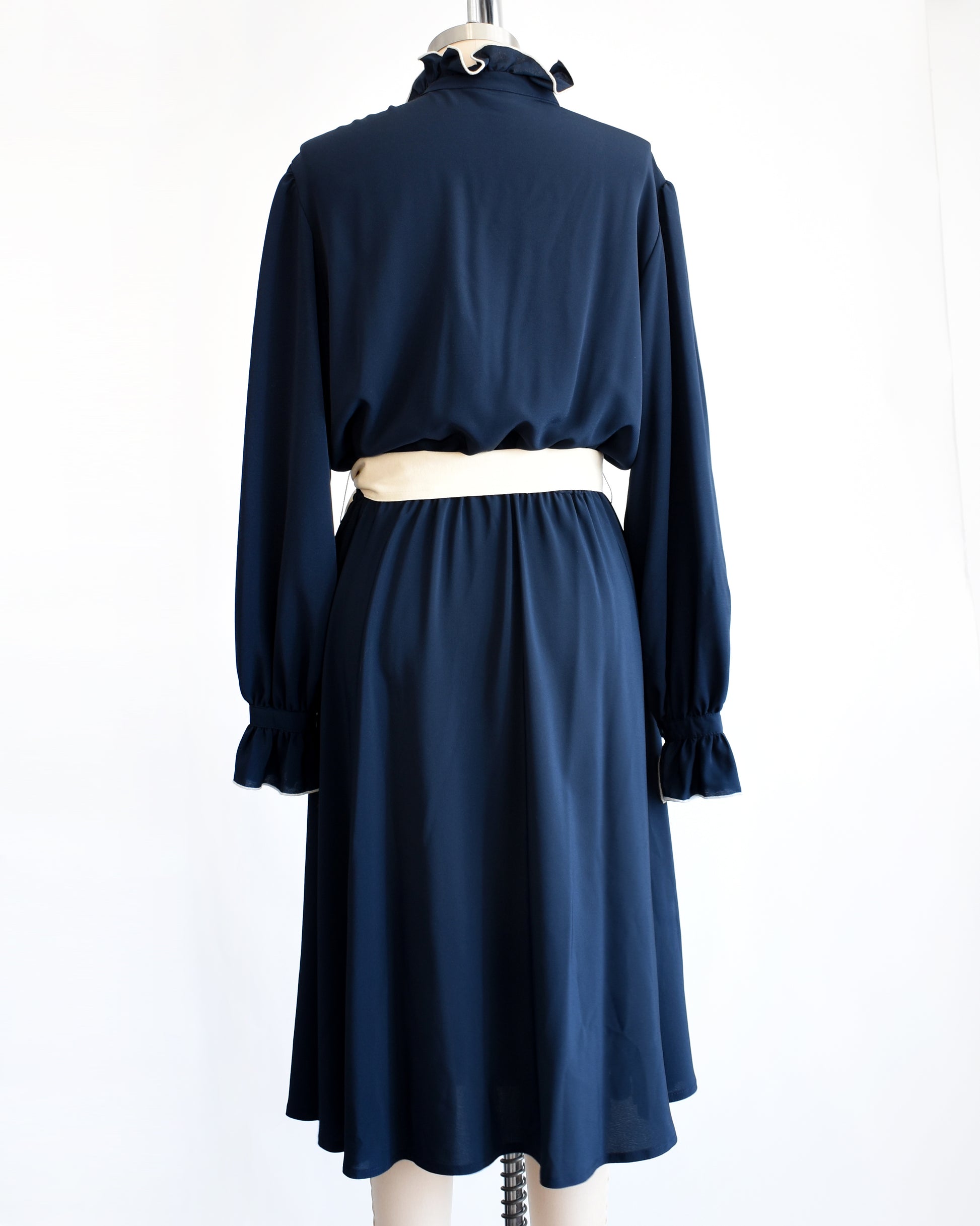 back view of a vintage late 1970s early 1980s navy ruffled dress with cream colored tie belt