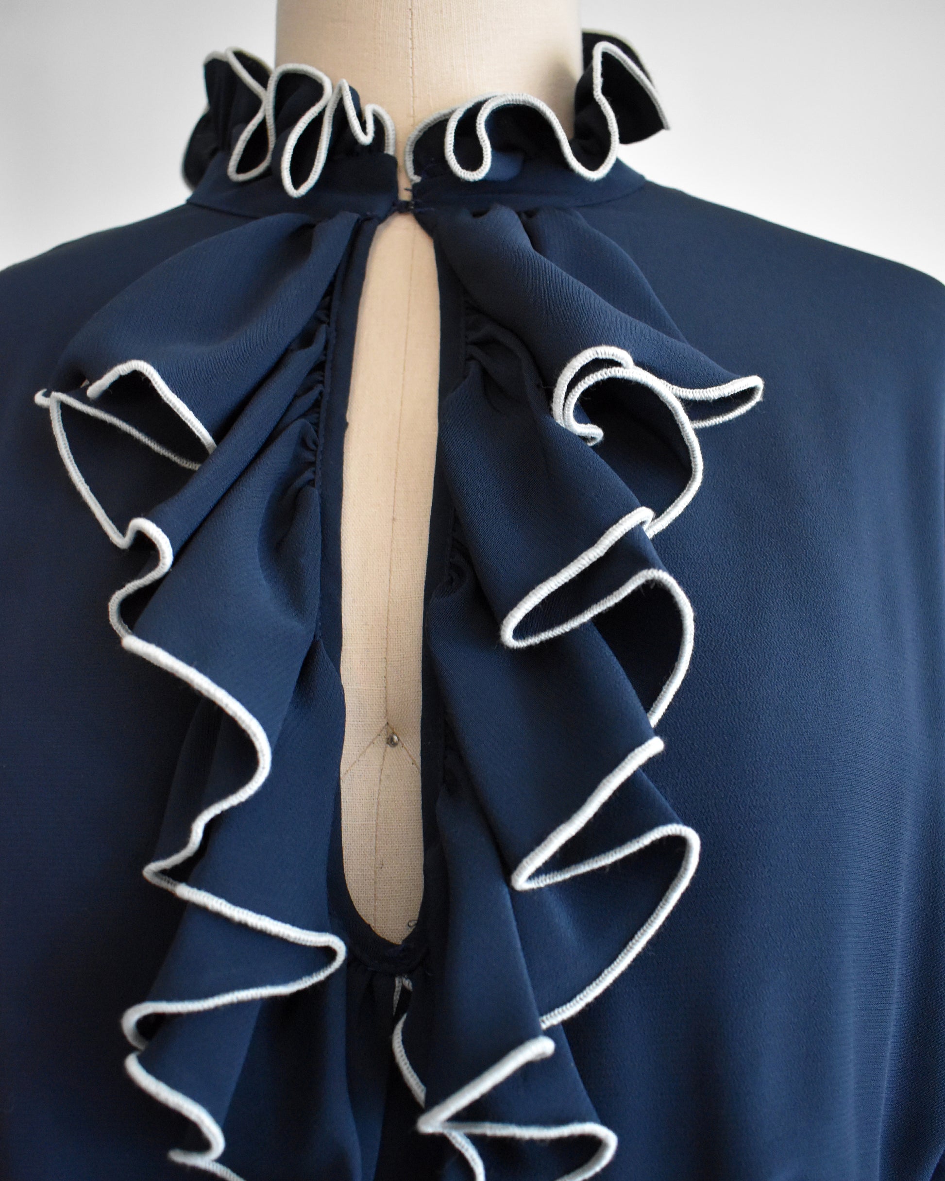 close up of the ruffled neckline and front of a vintage late 1970s early 1980s navy ruffled dress with cream colored tie belt