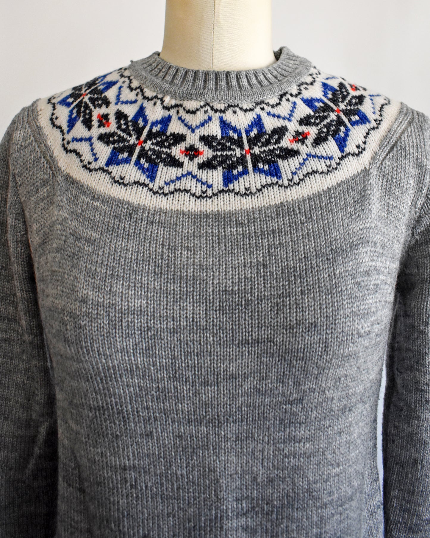 close up of the collar on a vintage 70s gray sweater with snowflake patterned neckline on a mannequin against a white background