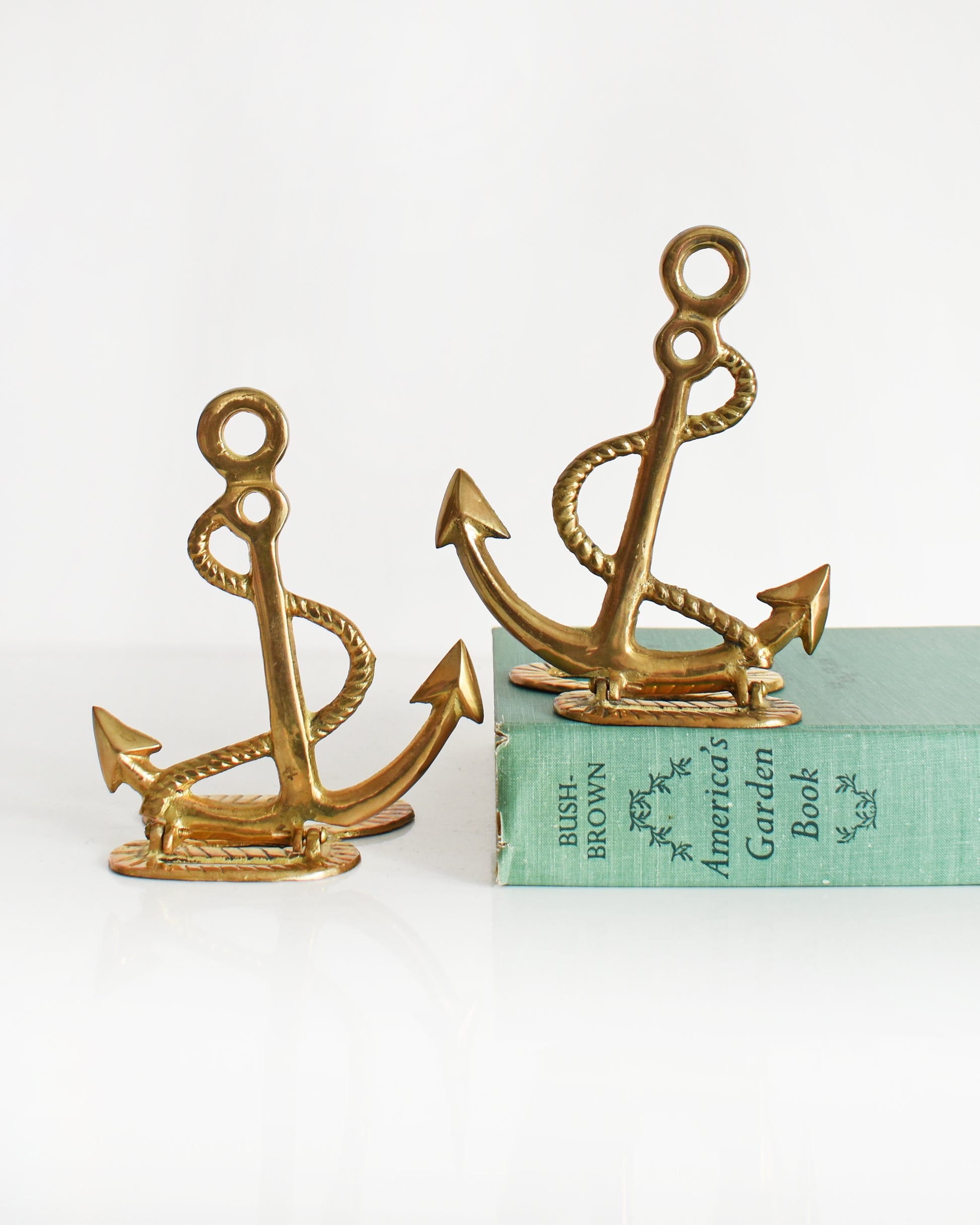 Two vintage brass anchor and rope bookends. One of the bookends is on a green book