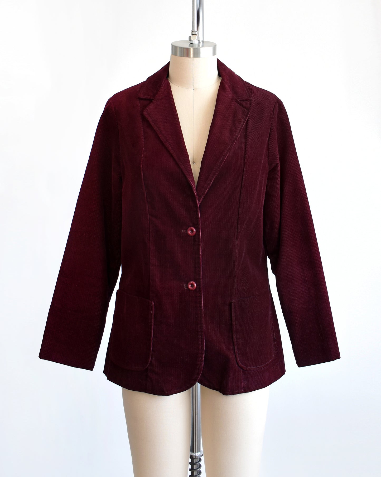 A vintage 1980s burgundy corduroy blazer that features two plastic buttons on the front and two front patch pockets on each side.