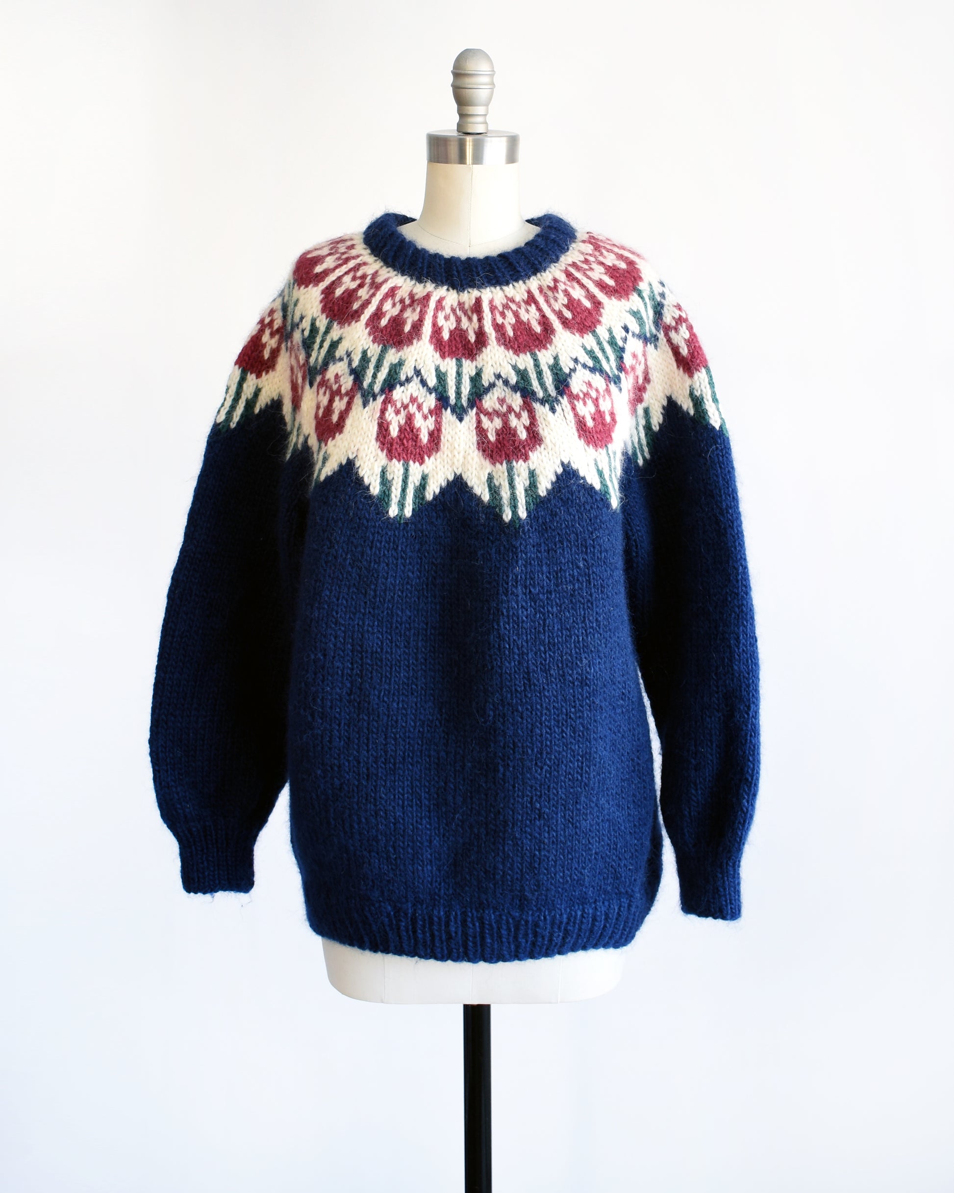 A vintage 1980s navy blue Fair Isle sweater that features a dark pink and green tulip pattern around the collar.