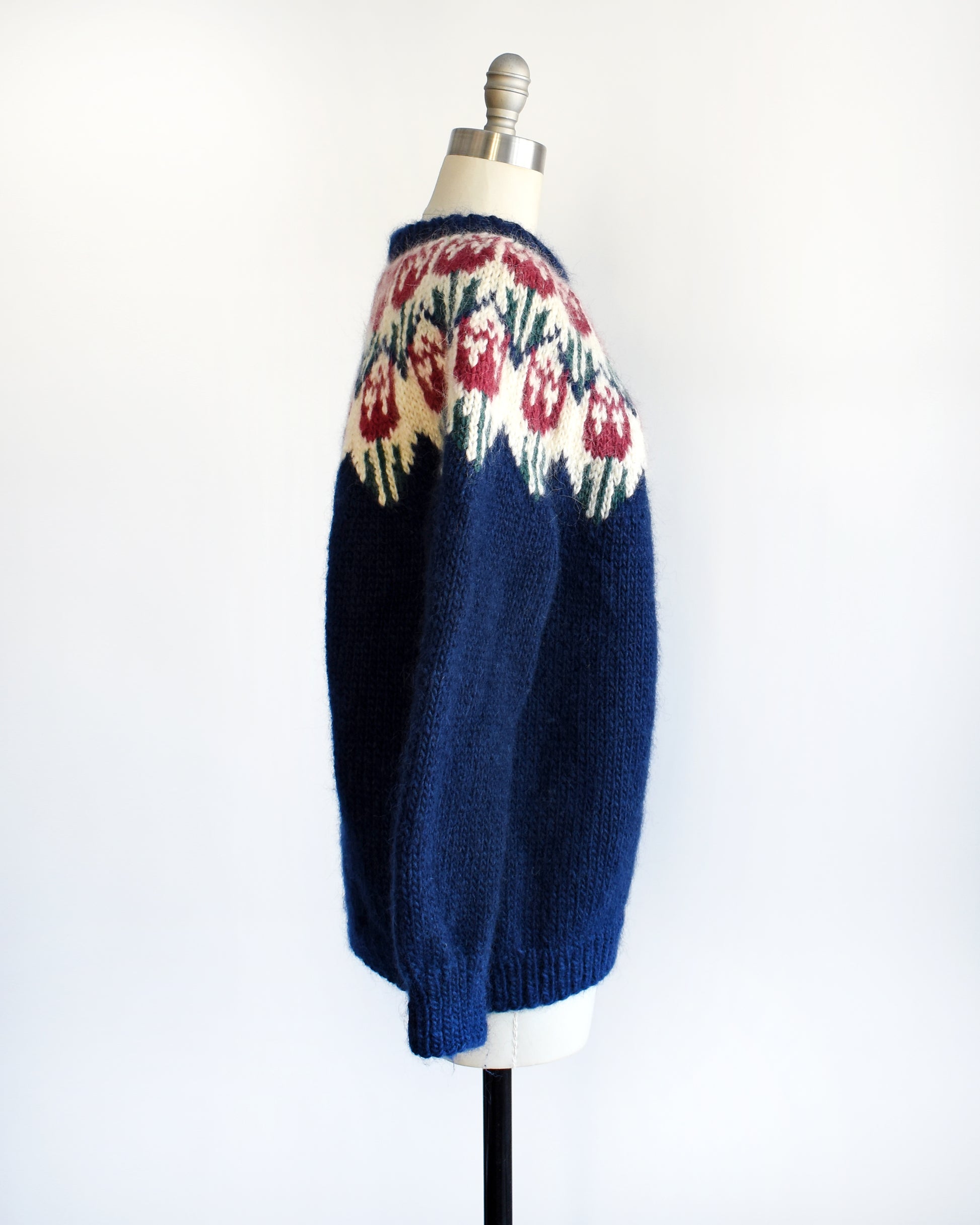 Side view of a vintage 1980s navy blue Fair Isle sweater that features a dark pink and green tulip pattern around the collar.