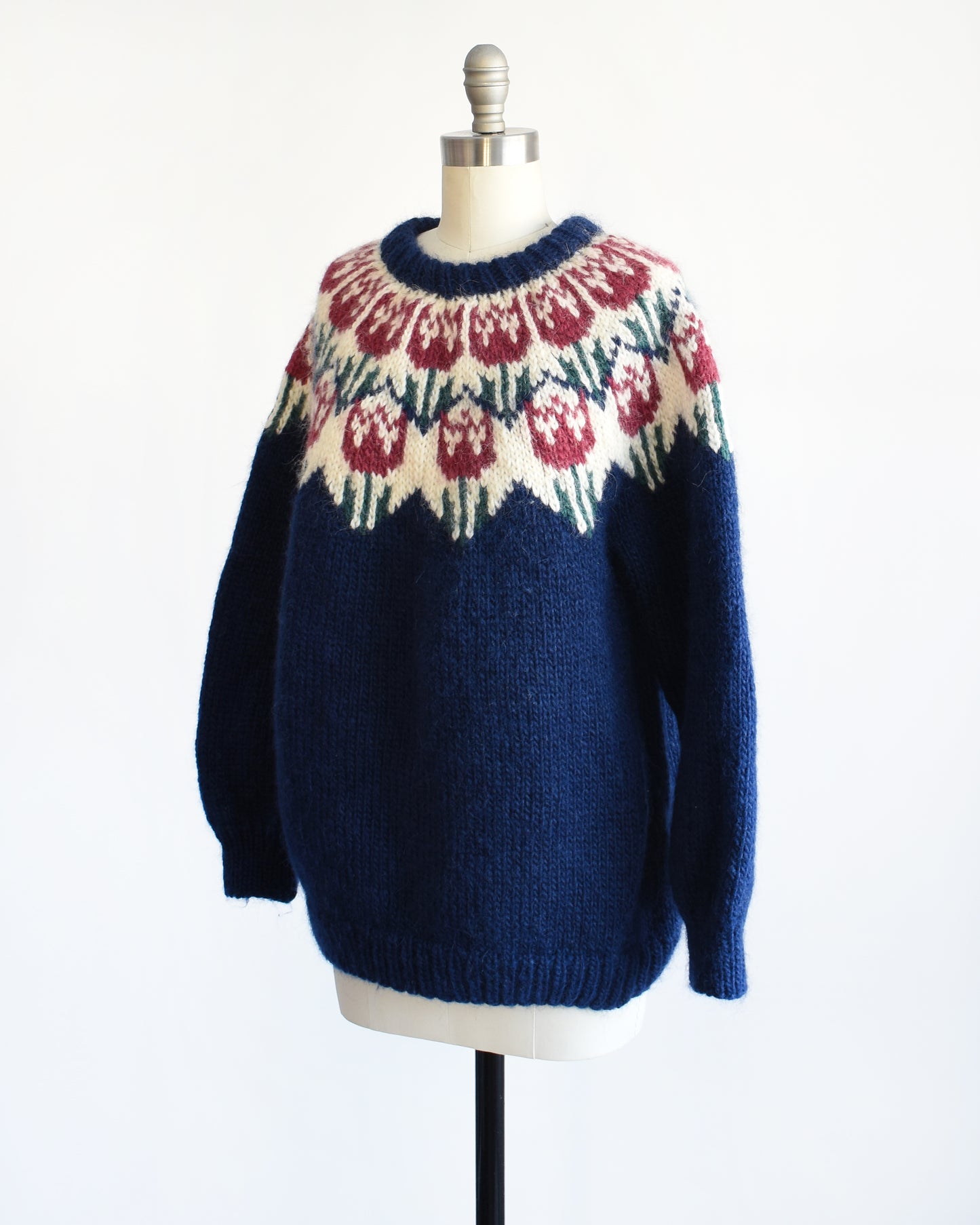 Side front view of a vintage 1980s navy blue Fair Isle sweater that features a dark pink and green tulip pattern around the collar.