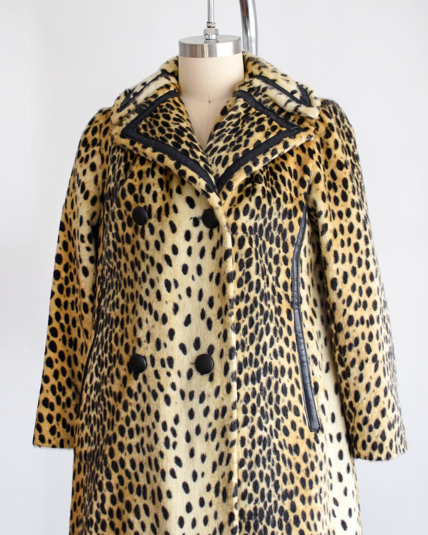 Side front view of a faux fur cheetah print coat features golden faux fur with black spots and black faux leather trim