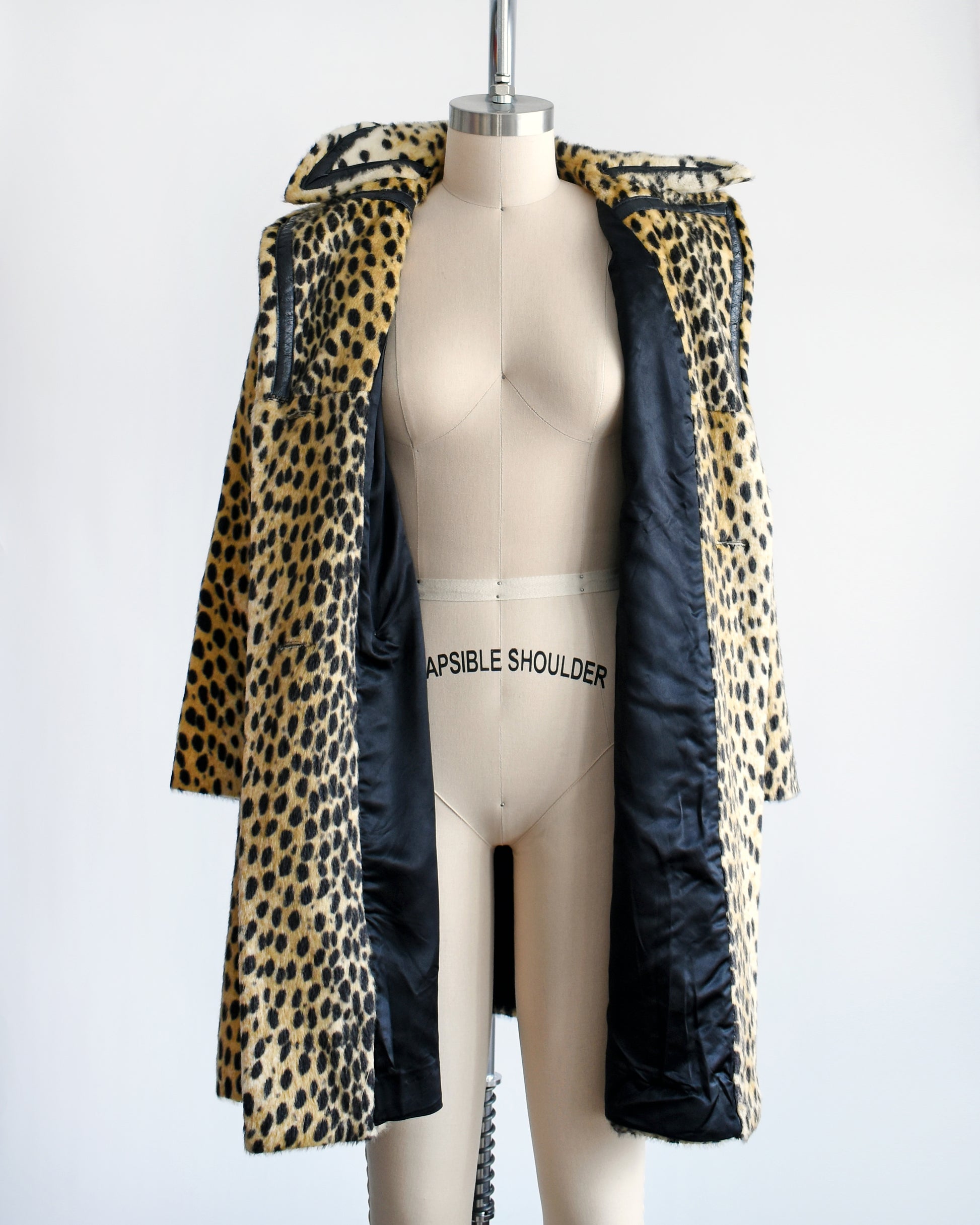 A faux fur cheetah print coat features golden faux fur with black spots and black faux leather trim. The coat is open in this photo showing the black lining.