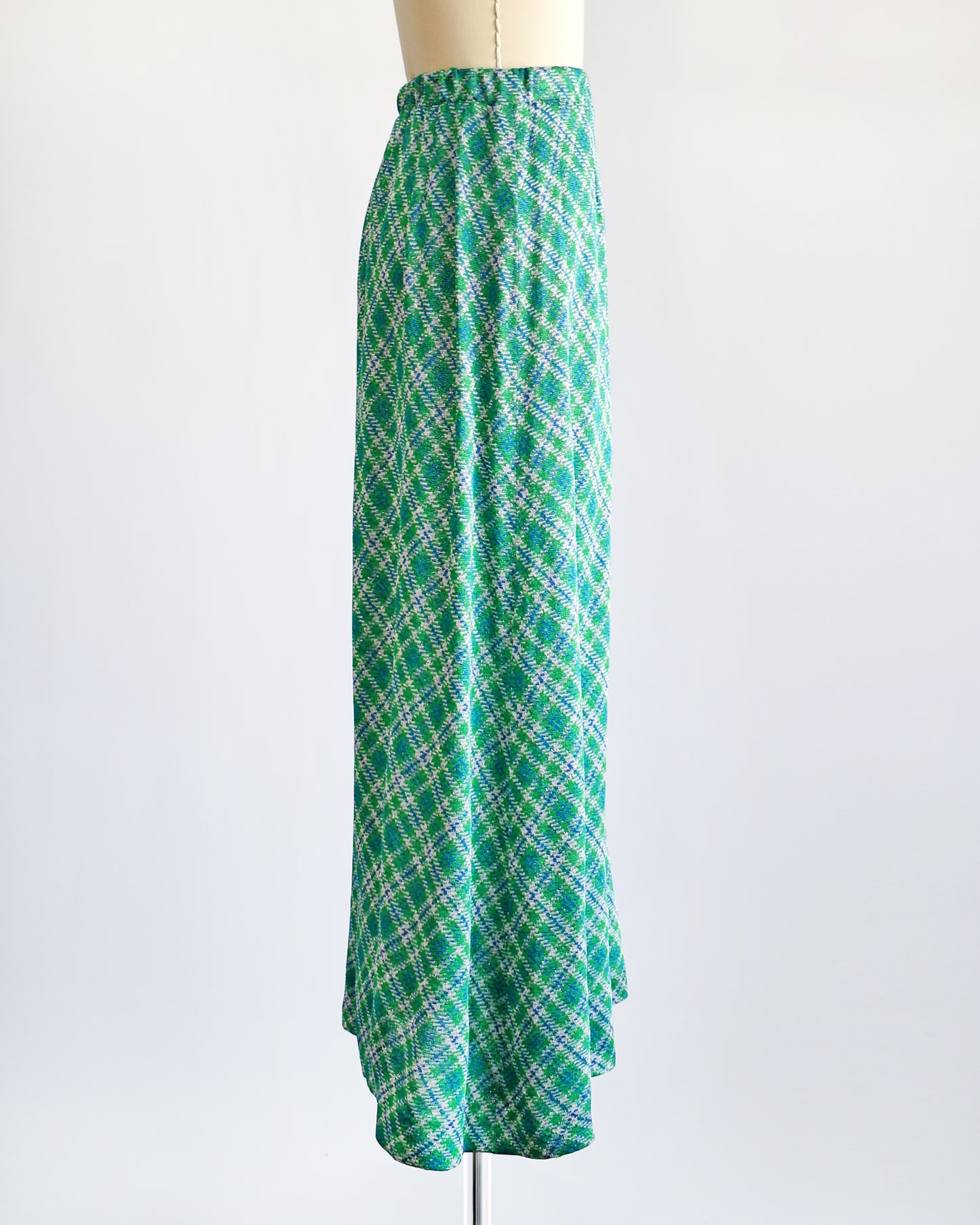 Side view of a vintage 1970s maxi skirt that features festive green, blue, and white plaid fabric with silver metallic threads.