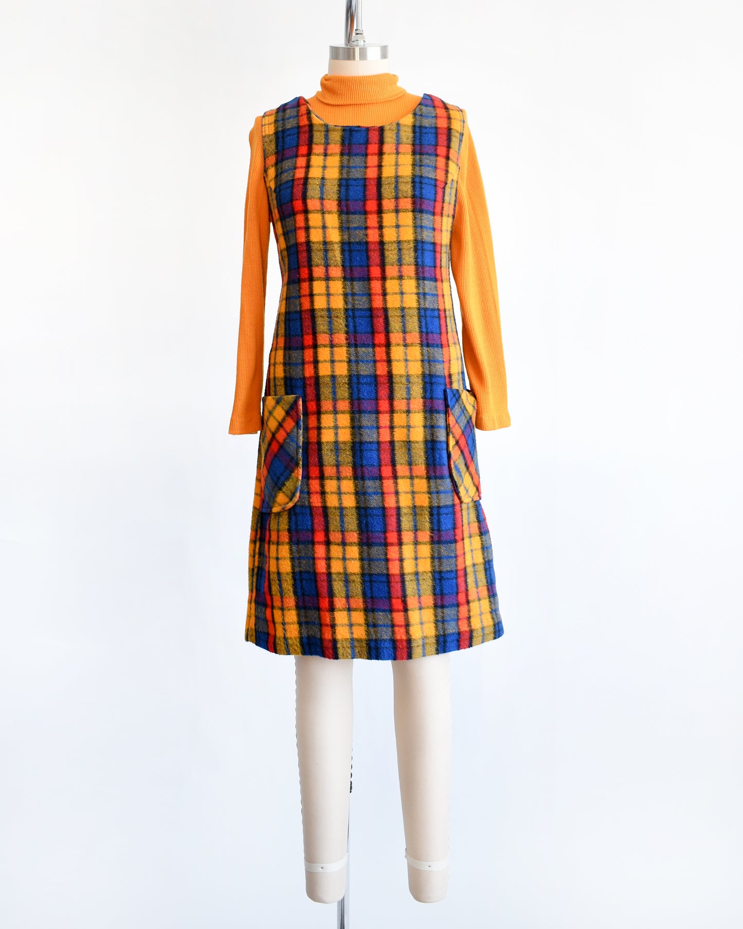 A vintage 1970s orange, blue, and red plaid pinafore dress with an orange turtleneck underneath