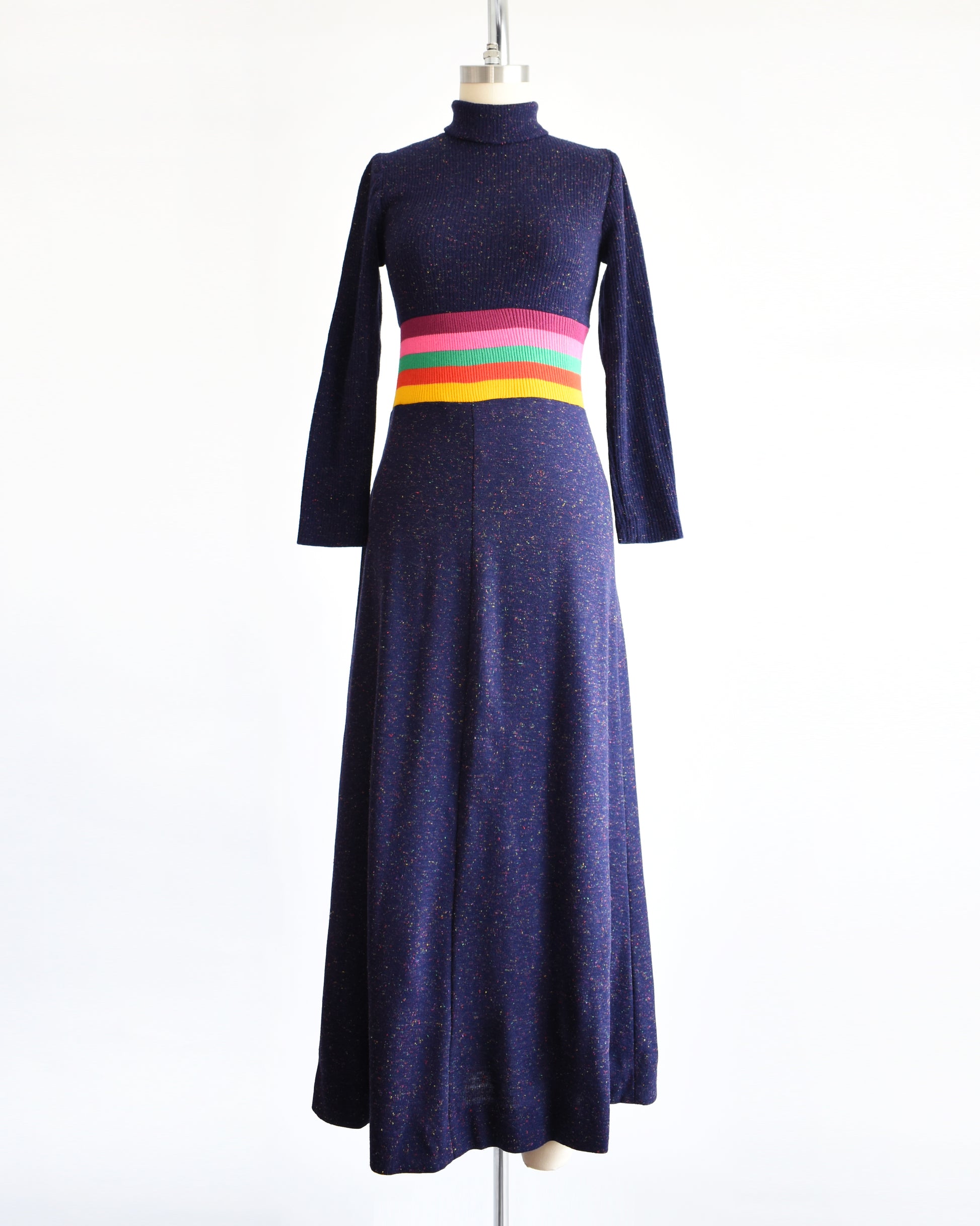 a vintage 1970s purple blue dress with a colorful striped waistband on a mannequin against a white background