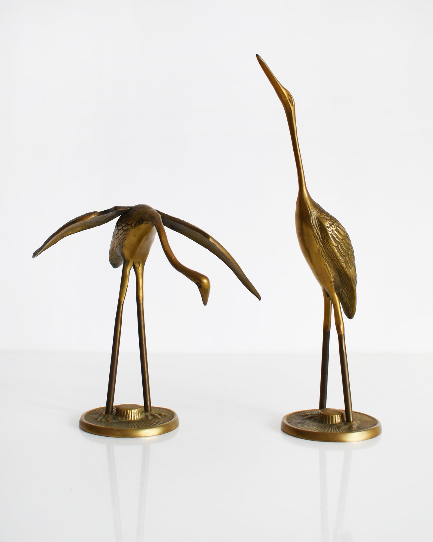 A pair of vintage brass cranes that have ornate carved detail on their wings and body.