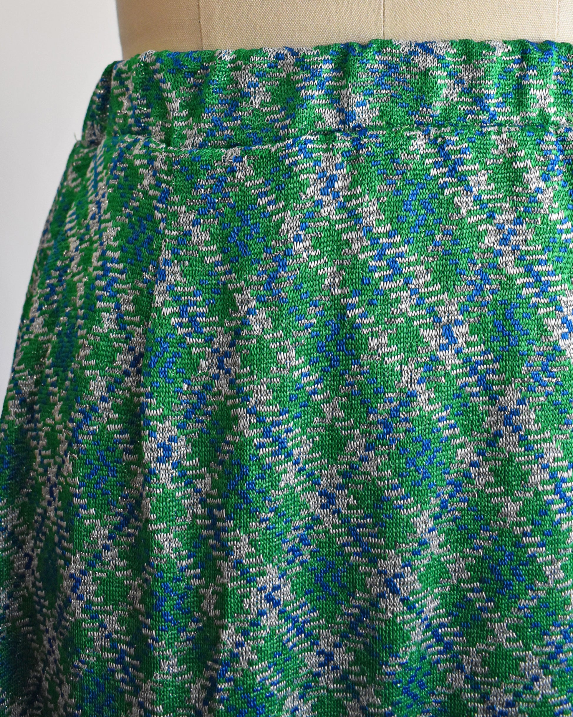 Close up of the waist and hip area of a vintage 1970s maxi skirt that features festive green, blue, and white plaid fabric with silver metallic threads.