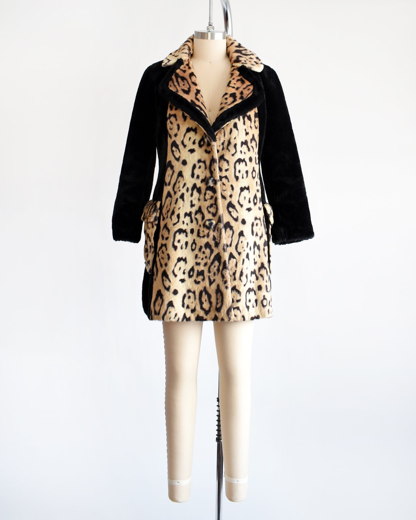 A vintage late 1960s early 1970s leopard faux fur coat that has large leopard print on the collar, down the front, and on the large side pockets. Black plush long sleeves, sides, and back. Matching black trim on the collar