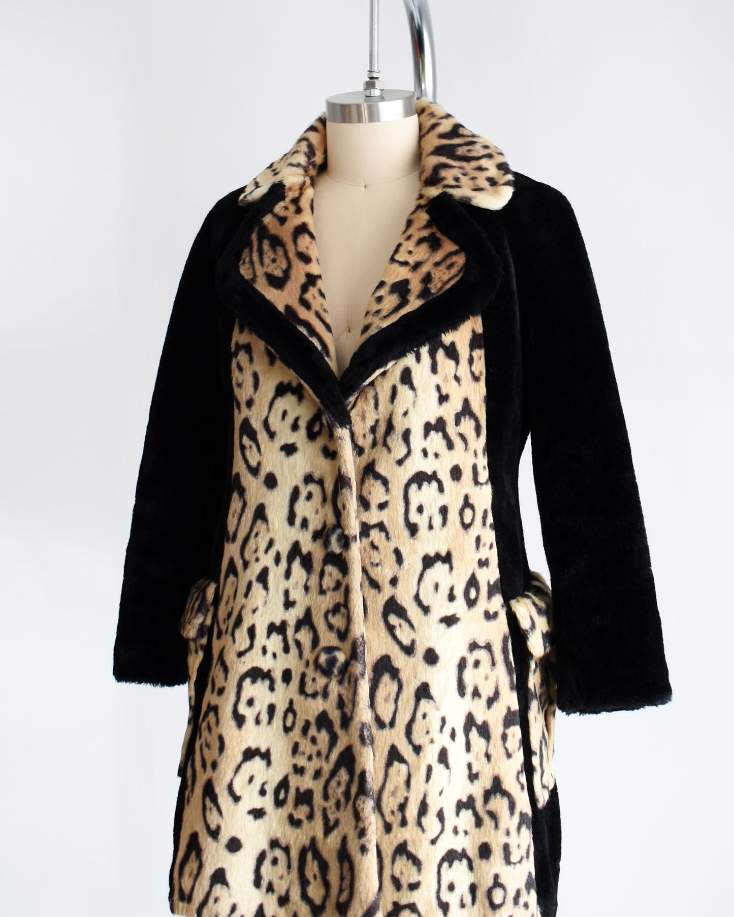 Side front view of a vintage late 1960s early 1970s leopard faux fur coat that has large leopard print on the collar, down the front, and on the large side pockets. Black plush long sleeves, sides, and back. Matching black trim on the collar