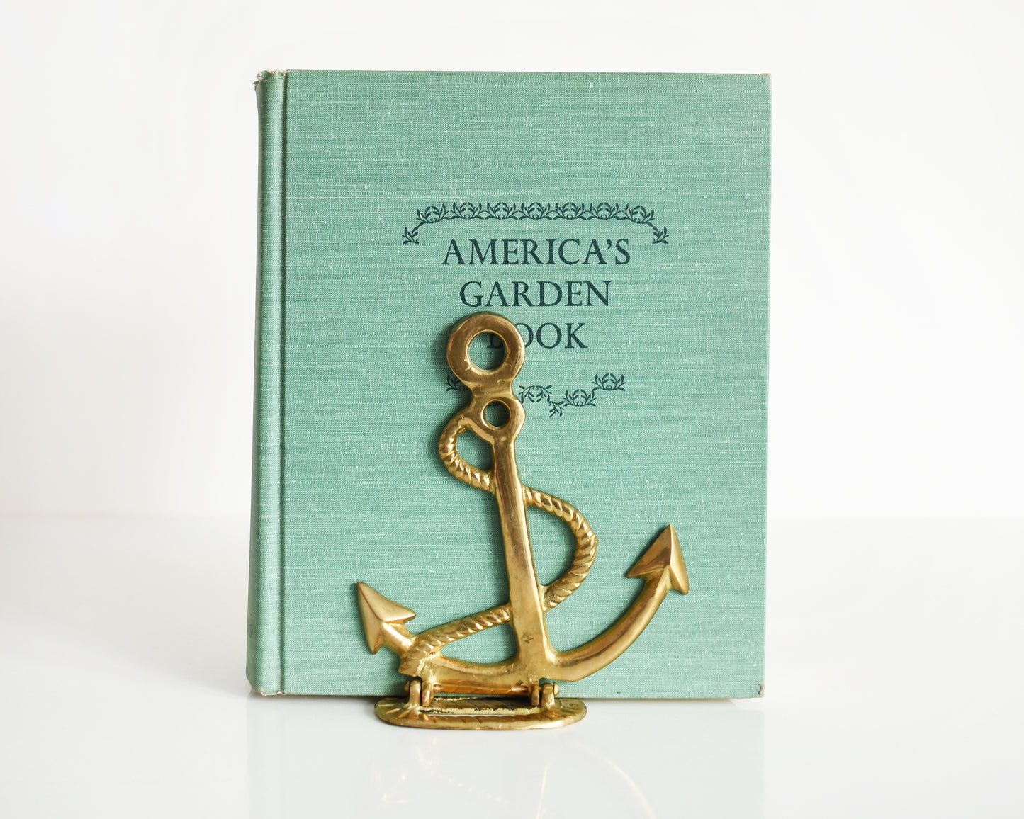 One vintage brass anchor and rope bookend that is holding up a green book