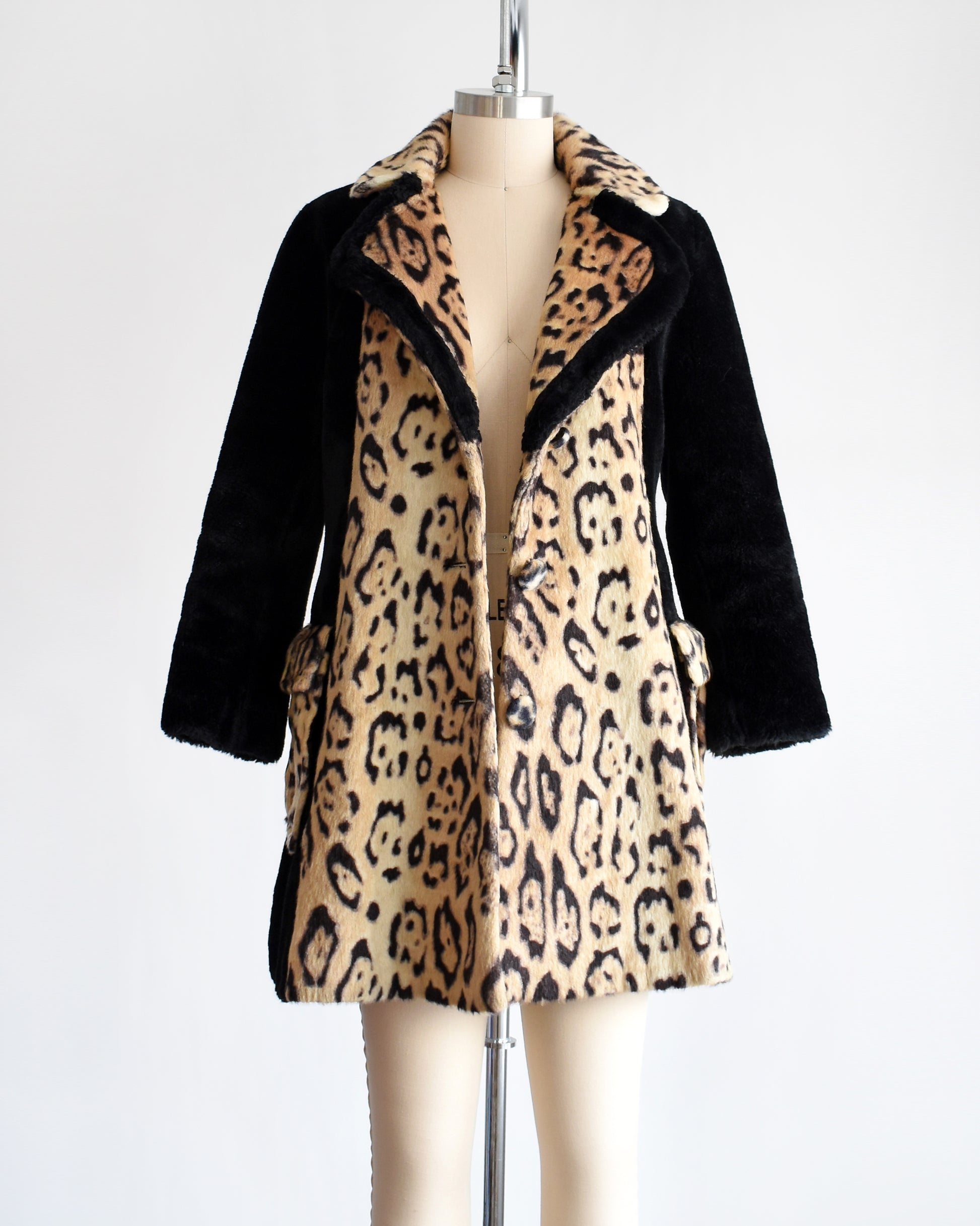 A vintage late 1960s early 1970s leopard faux fur coat that has large leopard print on the collar, down the front, and on the large side pockets. Black plush long sleeves, sides, and back. Matching black trim on the collar. The coat is open in this photo.
