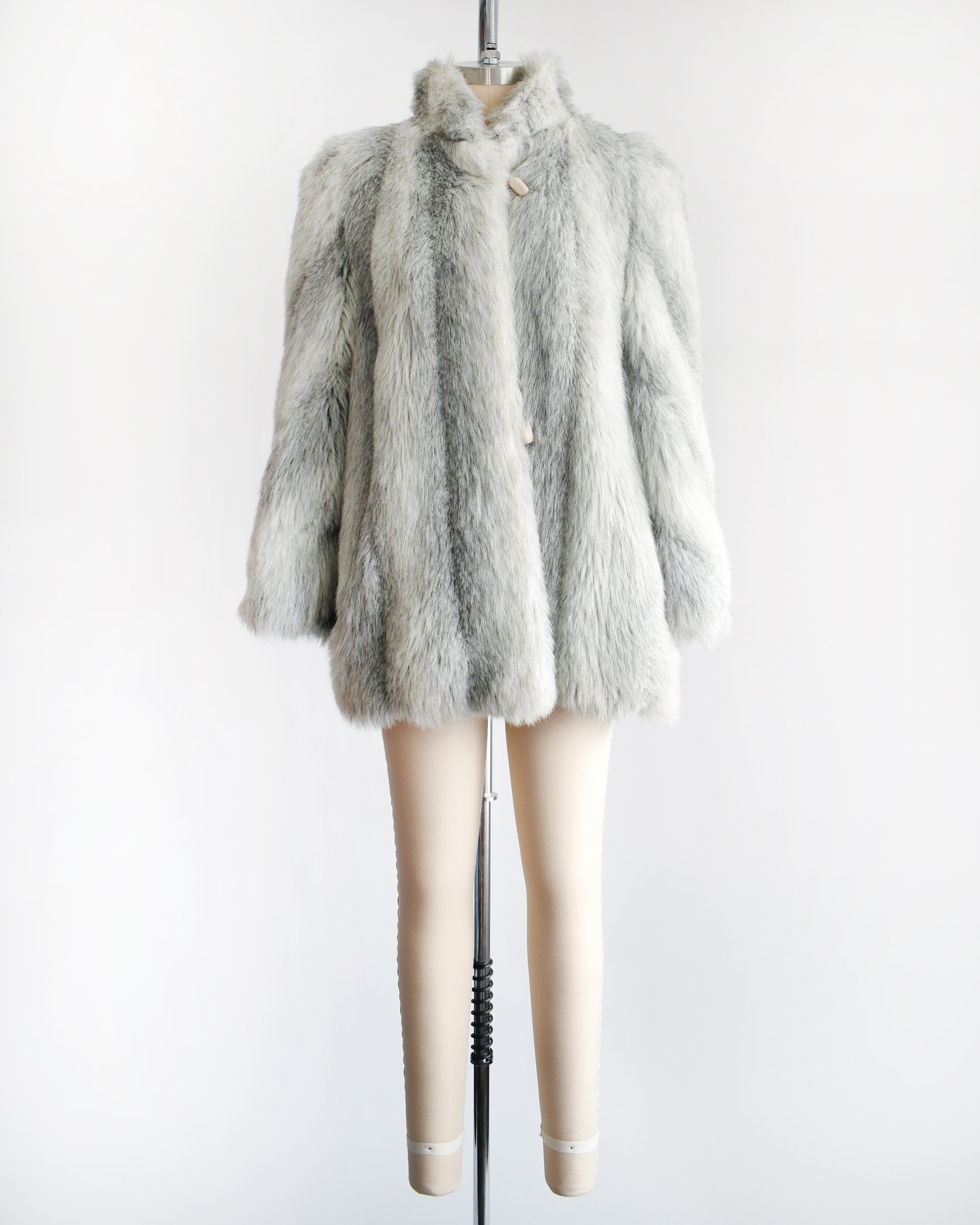 A vintage 1980s faux fur coat that features a plush white faux fur with light and dark gray stripes, a high collar, and structured puffed shoulders.