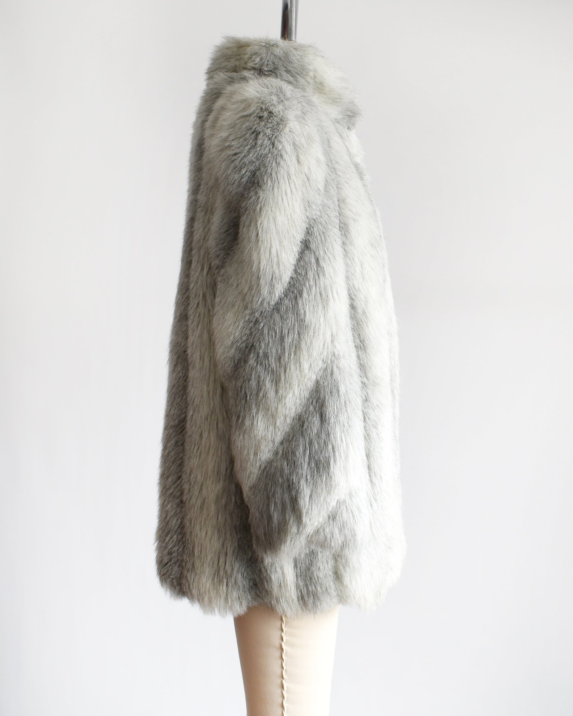 Side view of a vintage 1980s faux fur coat that features a plush white faux fur with light and dark gray stripes, a high collar, and structured puffed shoulders.