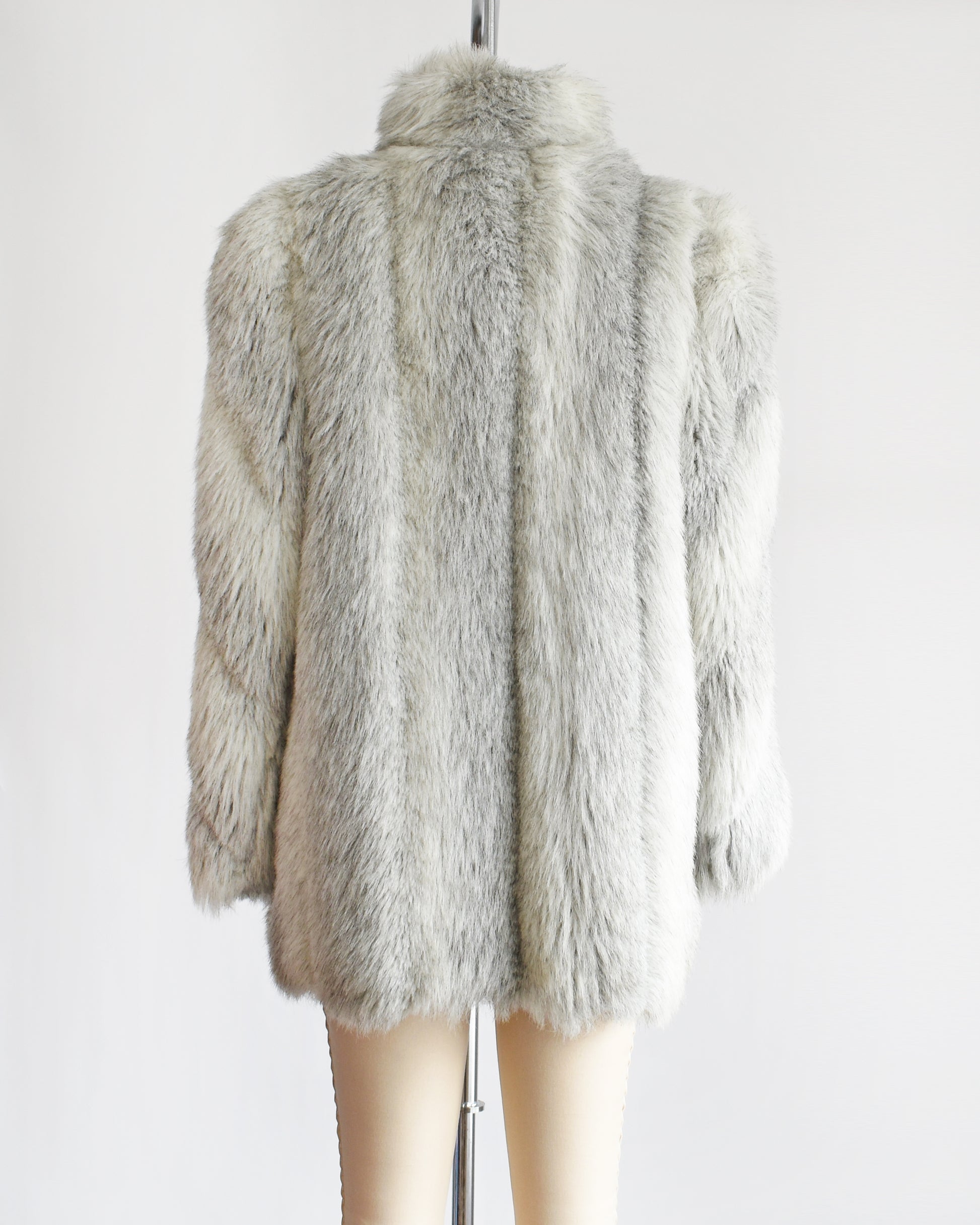 Back view of a vintage 1980s faux fur coat that features a plush white faux fur with light and dark gray stripes, a high collar, and structured puffed shoulders.