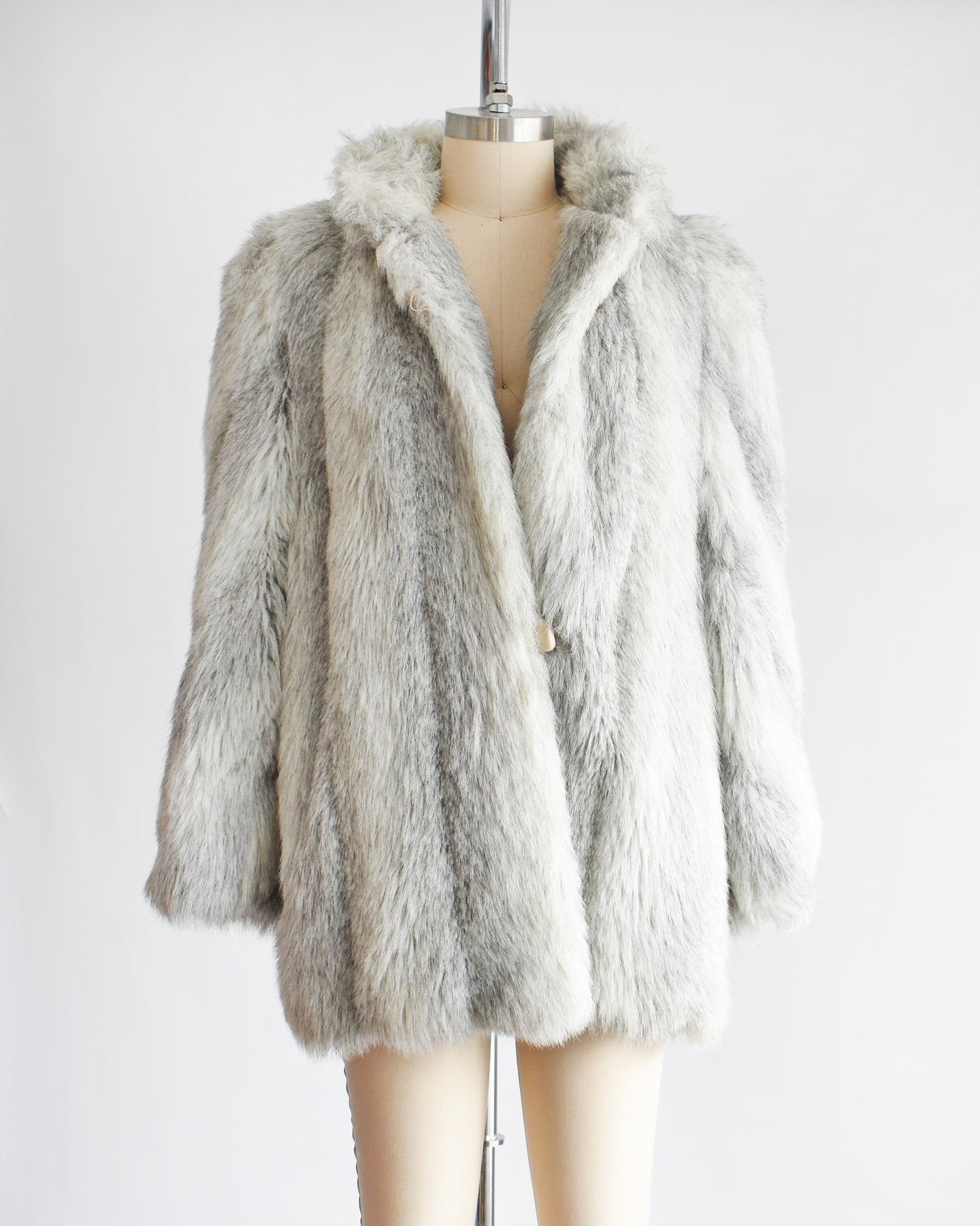 A vintage 1980s faux fur coat that features a plush white faux fur with light and dark gray stripes, a high collar, and structured puffed shoulders. The top button is unbuttoned.
