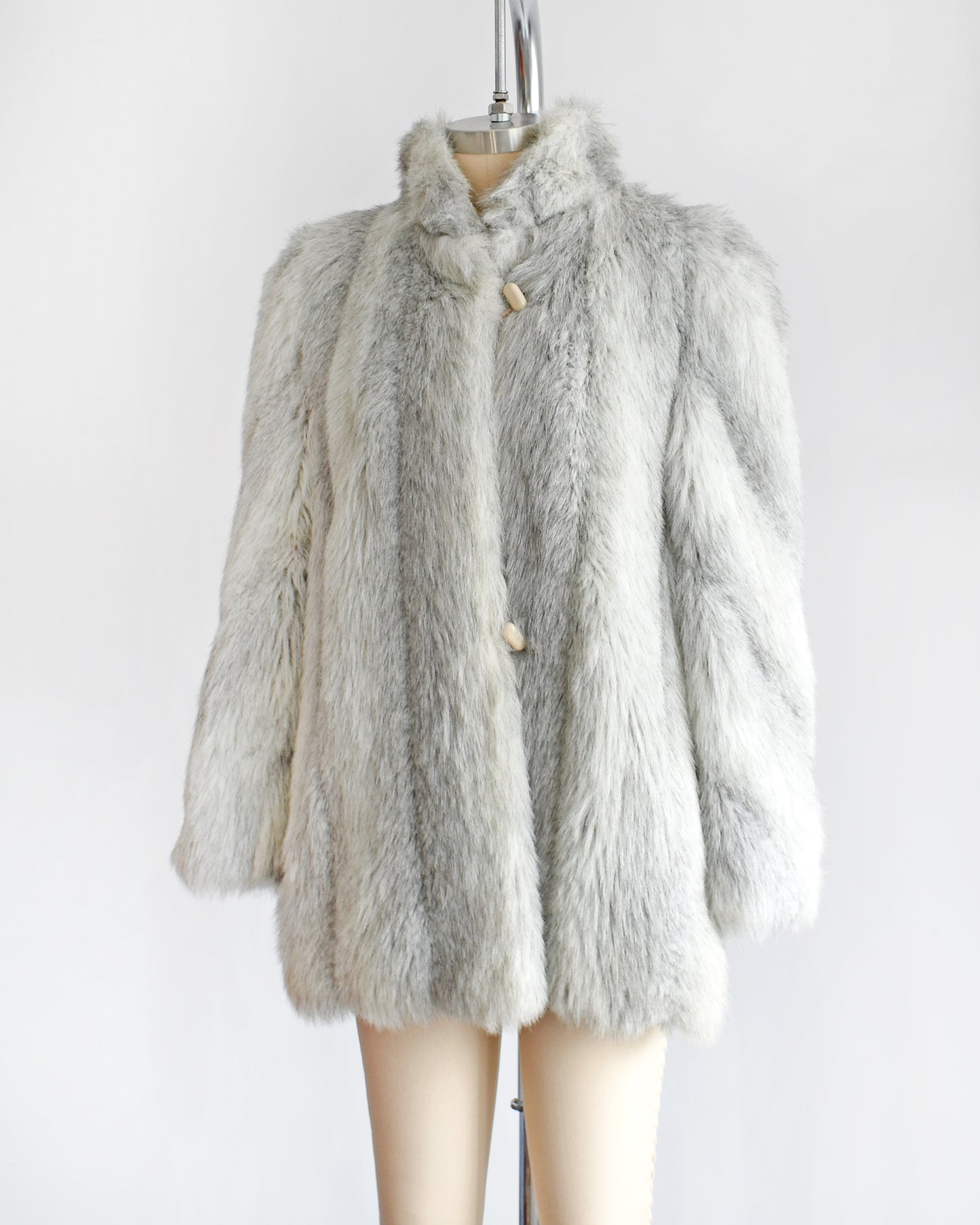 Side front view of a vintage 1980s faux fur coat that features a plush white faux fur with light and dark gray stripes, a high collar, and structured puffed shoulders.