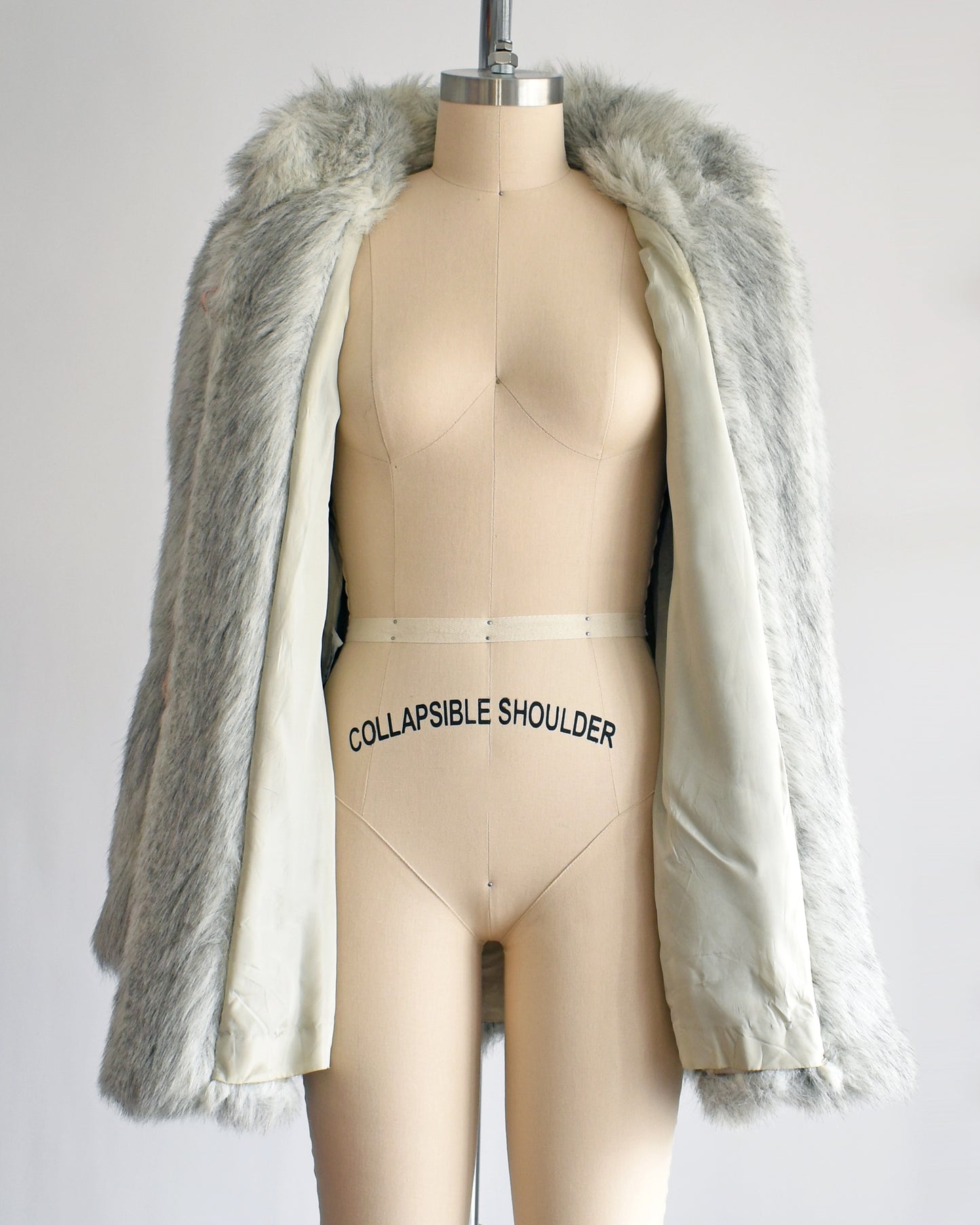 A vintage 1980s faux fur coat that features a plush white faux fur with light and dark gray stripes, a high collar, and structured puffed shoulders. The coat is unbuttoned showing the gray lining.