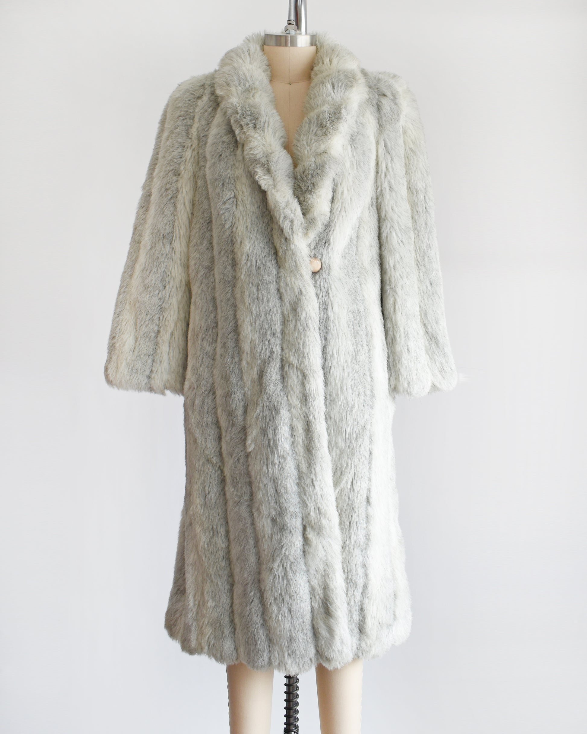 A vintage 1980s  cream colored faux fur coat with light and dark gray stripes.  The top button is unbuttoned in this photo.