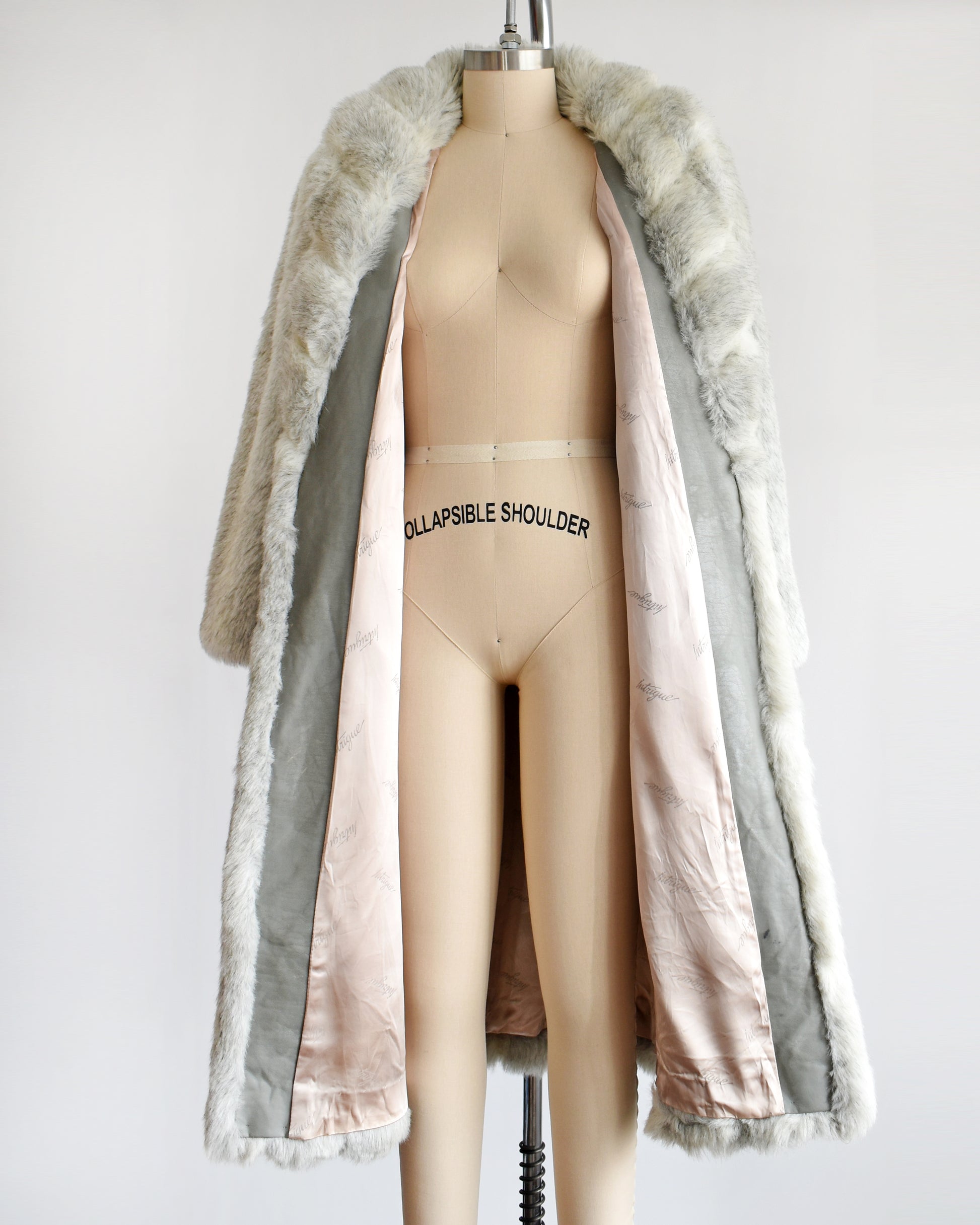 A vintage 1980s  cream colored faux fur coat with light and dark gray stripes.  The coat is open in this photo showing the light pink lining and gray faux leather inside trim.