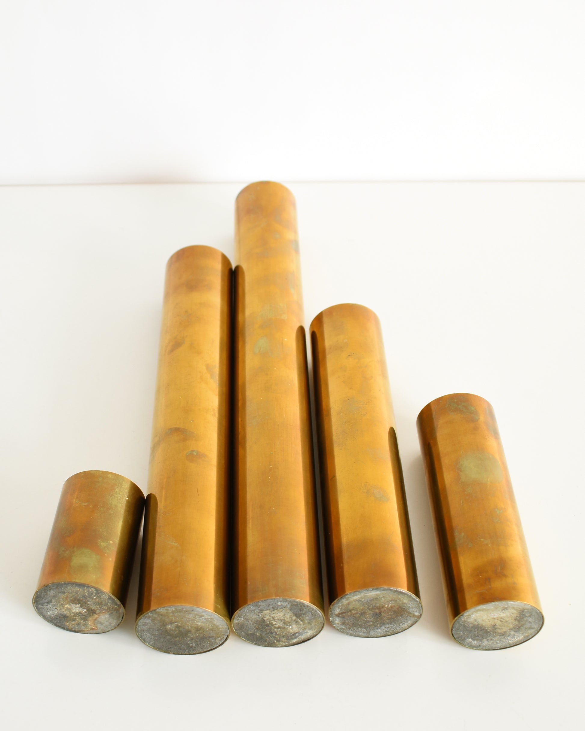 Overhead view of Five mid century brass cylindrical candle holders in different sizes. The bottoms are metal.