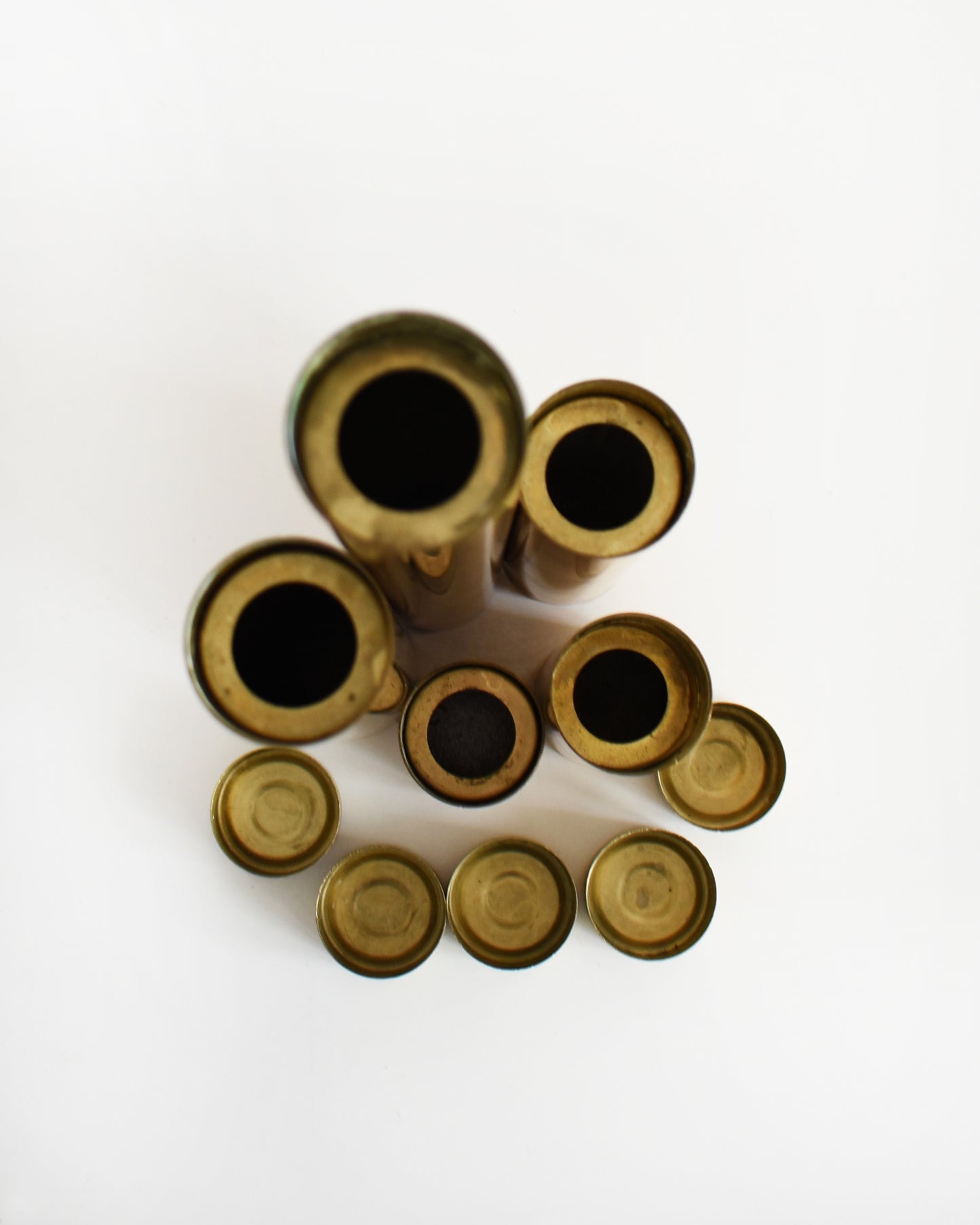 Overhead shot of Five mid century brass cylindrical candle holders in different sizes. The top candle inserts have been removed and are shown separately on the bottom.