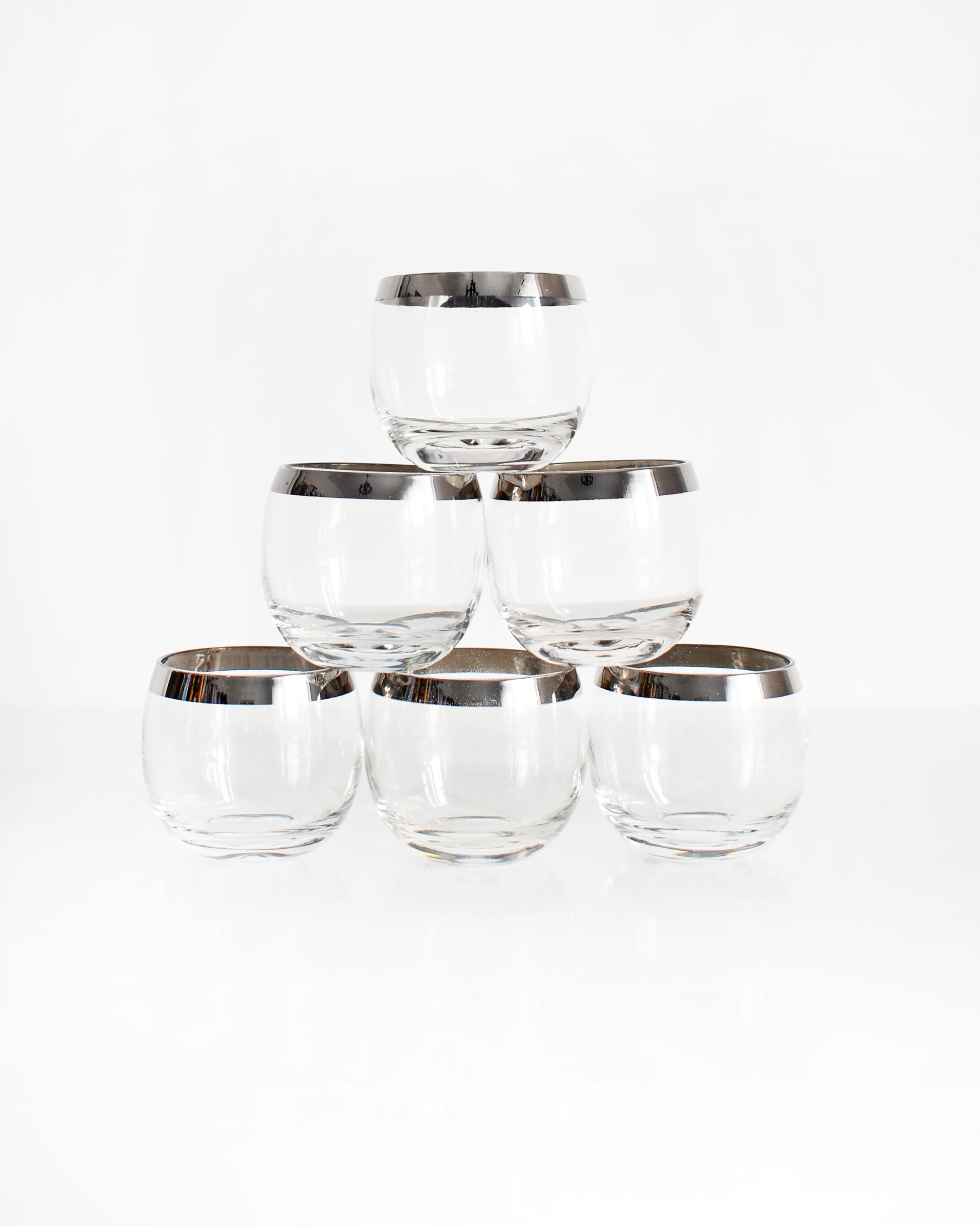 A set of six mid century roly poly glasses with silver rims. The glasses are in a stacked pyramid in this photo.
