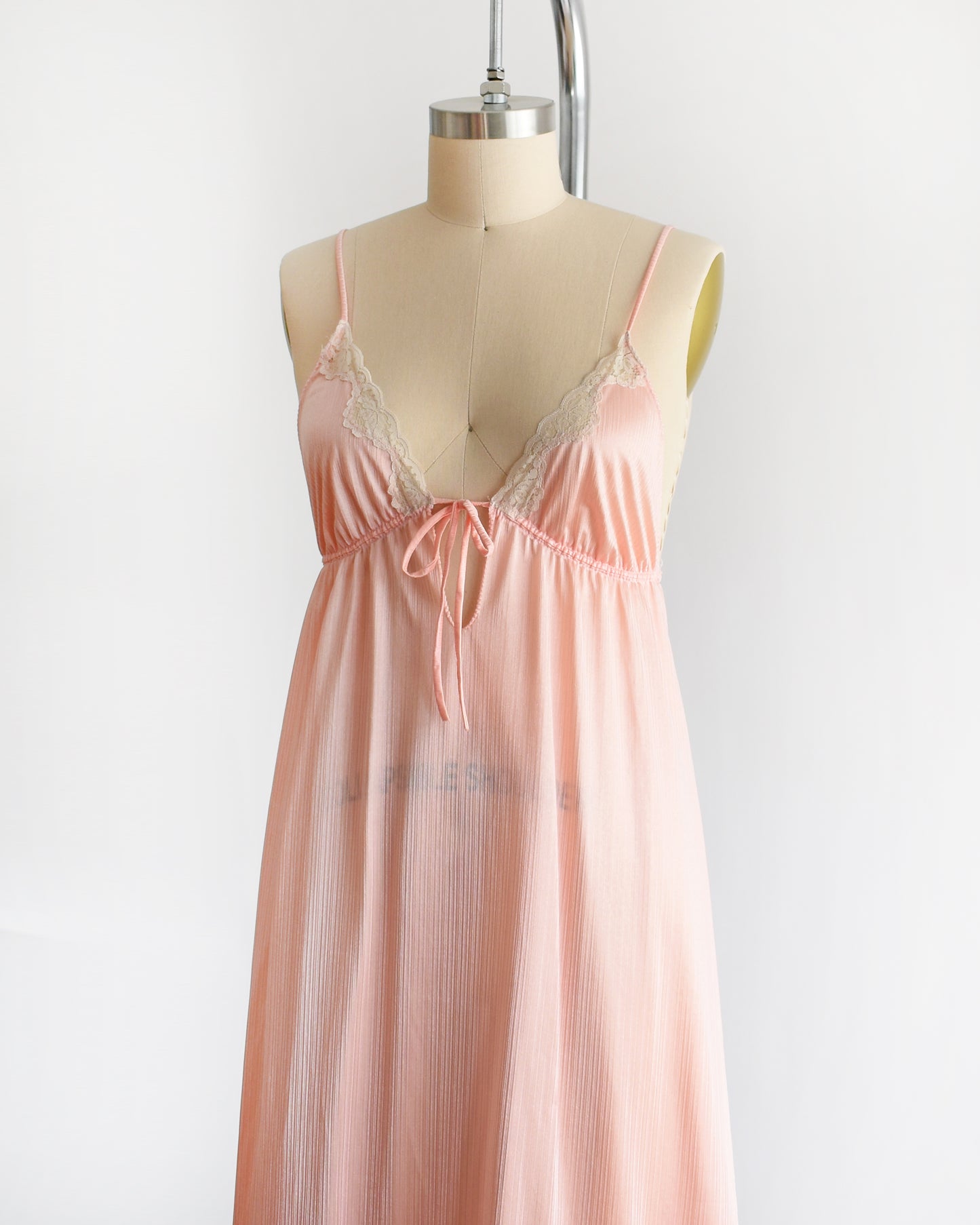 Side front view of a vintage 1970s peachy pink nightgown that has lace trim on the bodice